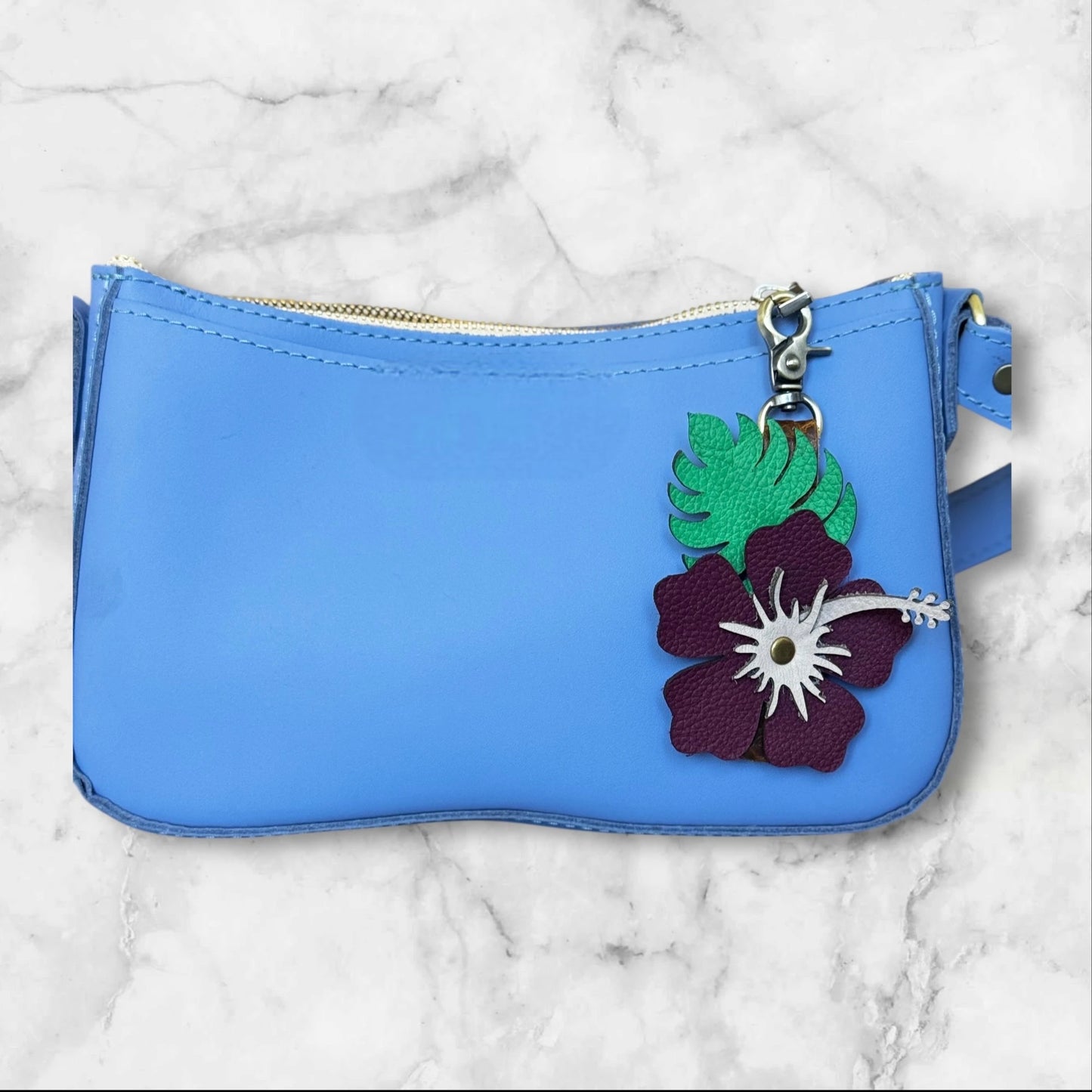Plum with blush stamen hibiscus leather flower with green monstera leaf for a tropical vibe on a blue bag on a marble counter top