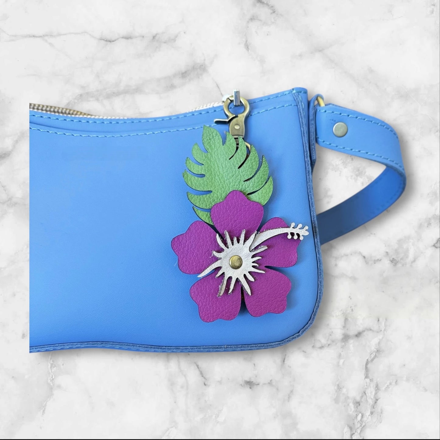 close up of Magenta with blush stamen leather hibiscus flower with matte green leaves on a blue bag