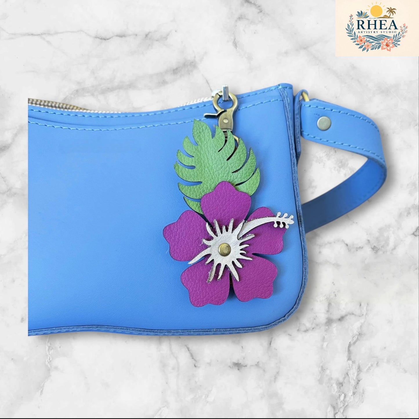 Magenta with blush stamen leather hibiscus flower with matte green leaves on a blue bag