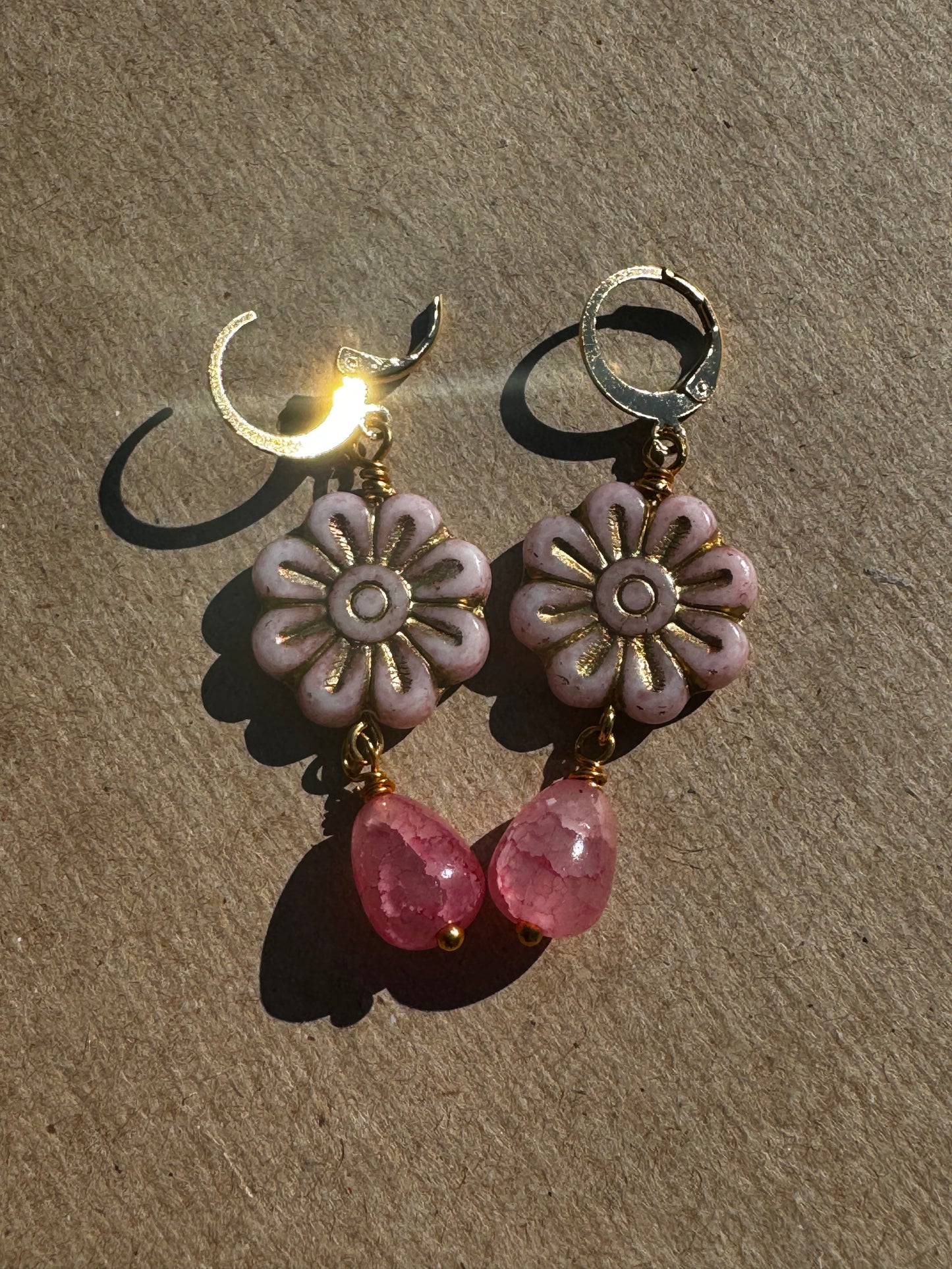 A pair of pale pink daisy-shaped earrings with gold wash and small pink gemstone accents, with gold plated brass findings.