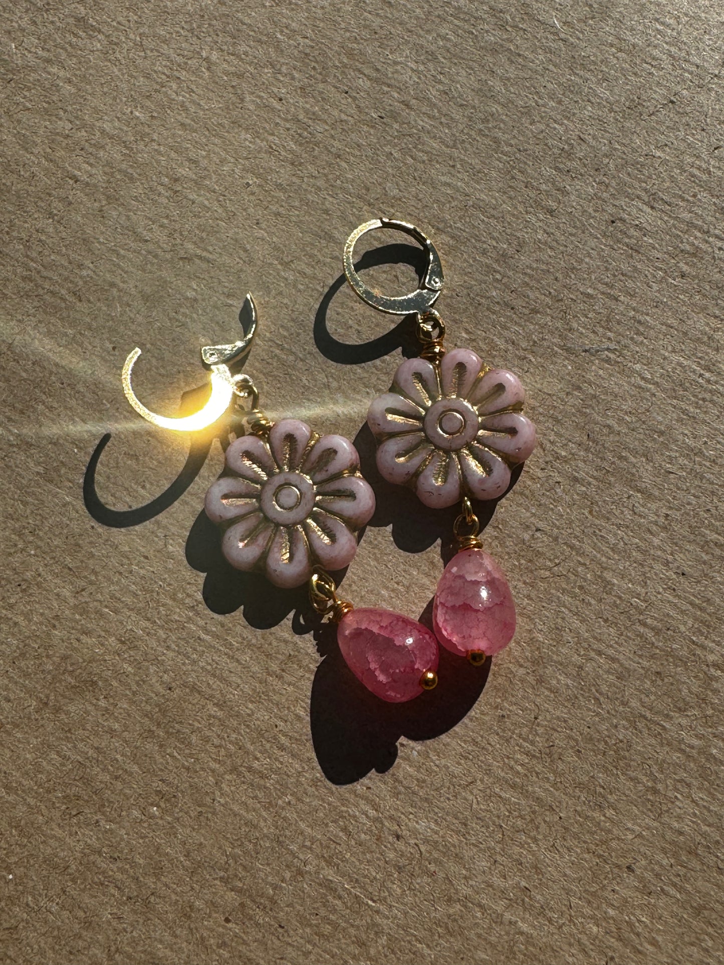 A pair of pale pink daisy-shaped earrings with gold wash and small pink gemstone accents, with gold plated brass findings.