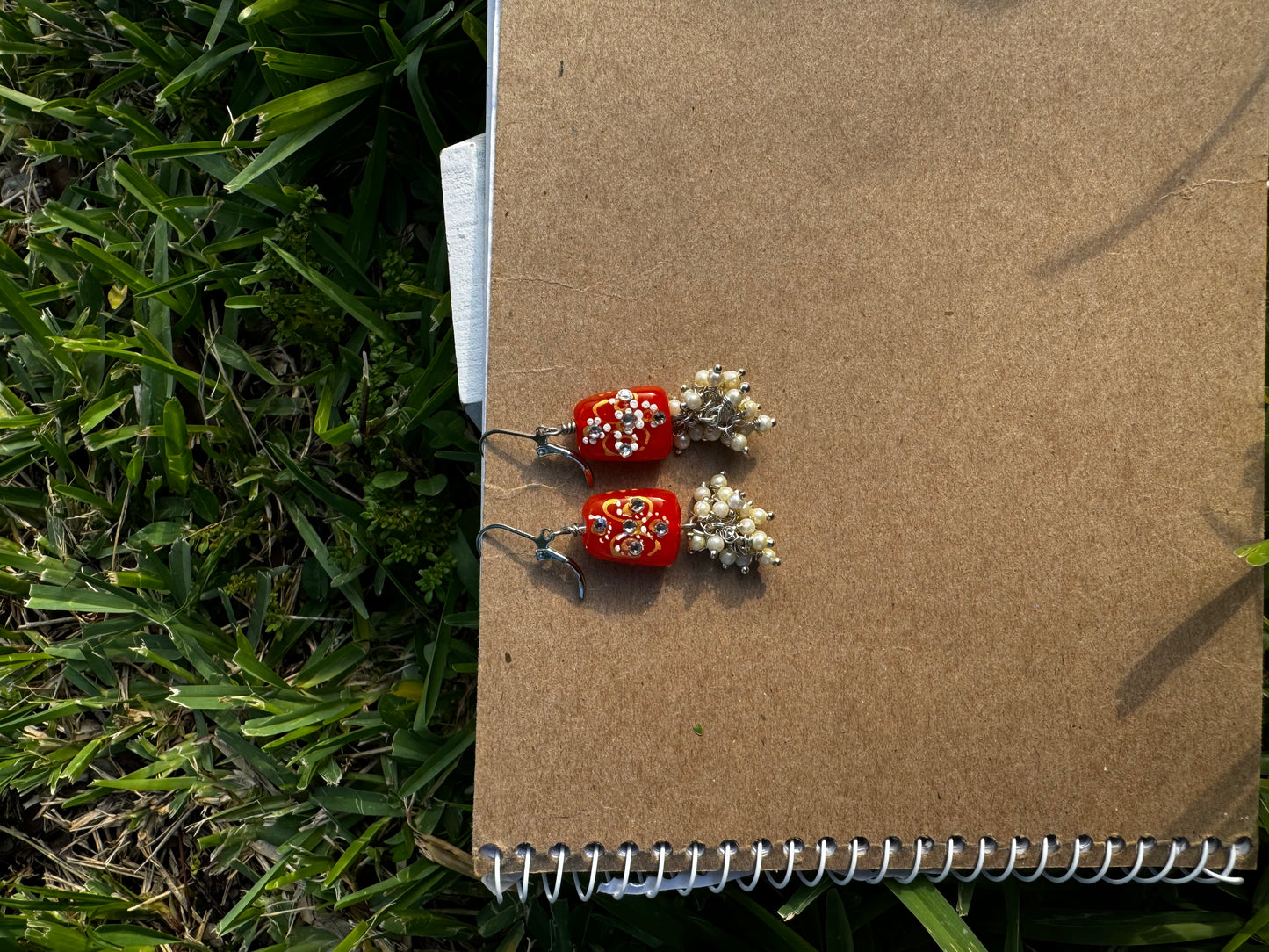 Red earrings with floral designs and pearl-like beads on a old book