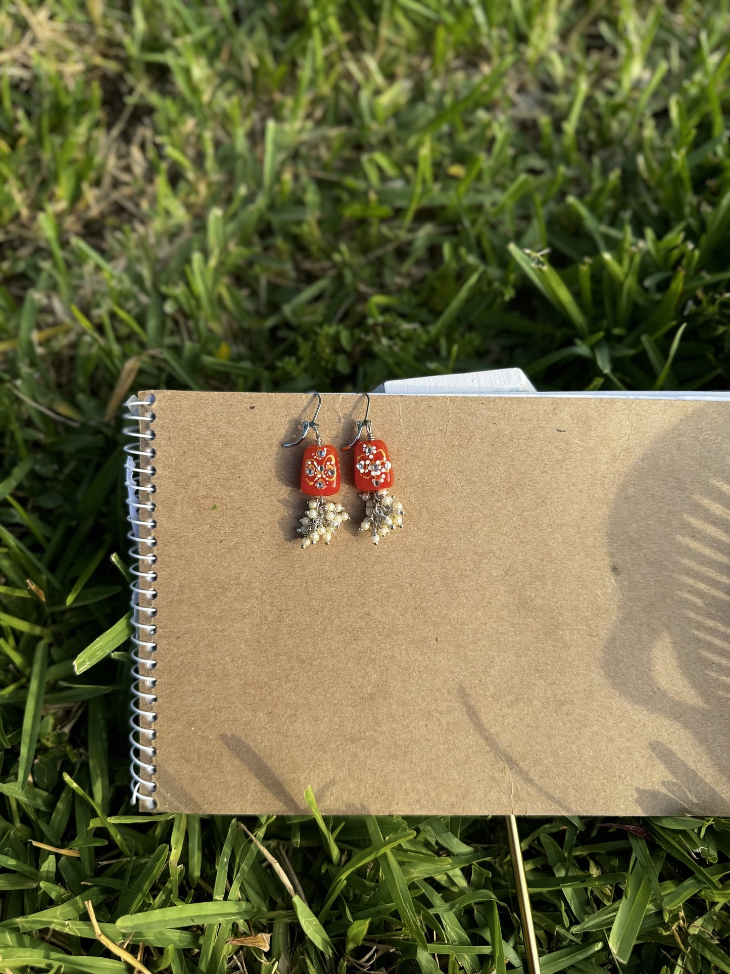 Red earrings with floral designs and pearl-like beads on a old book