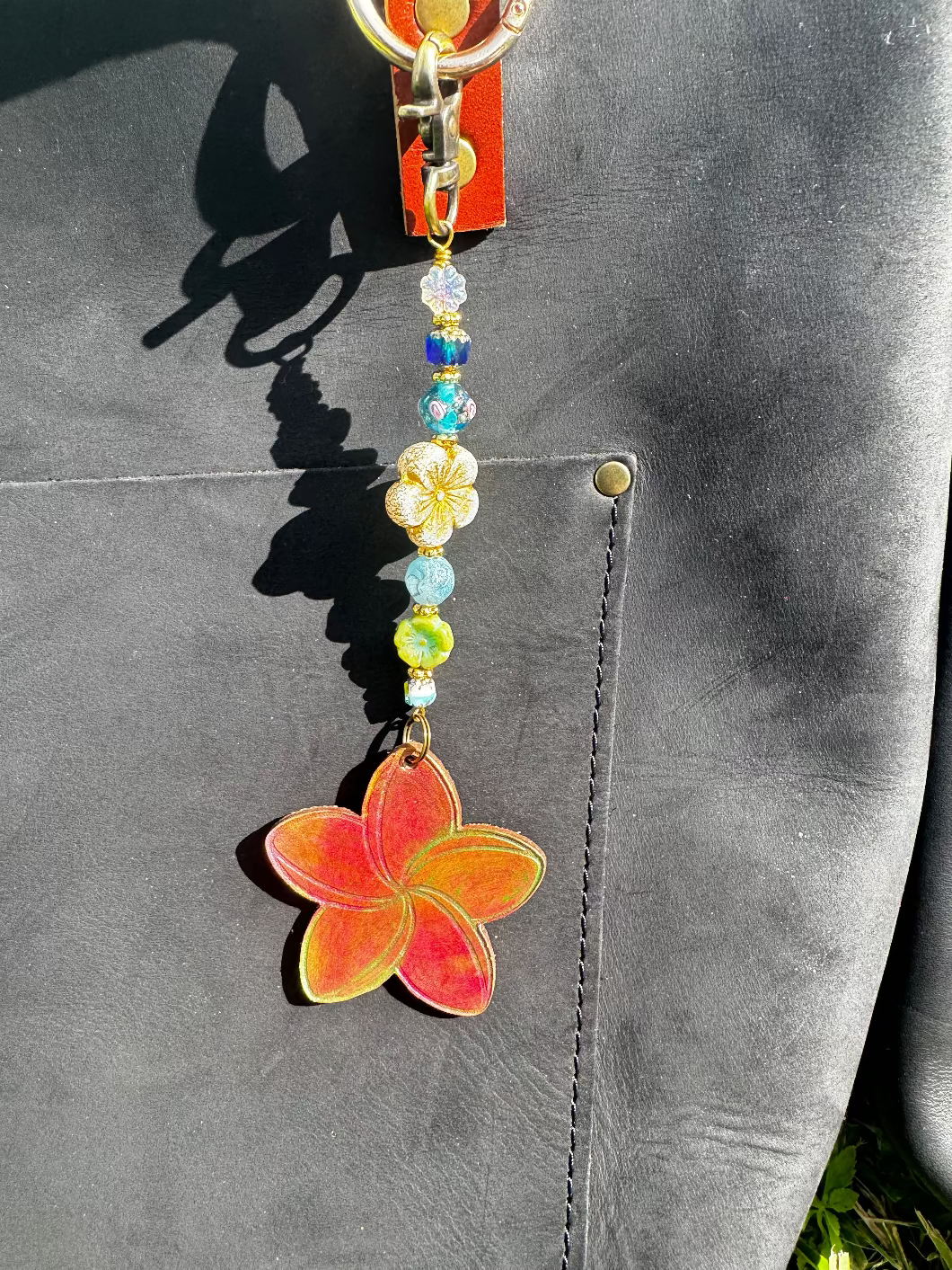 Decorative keychain with colorful beads and a red flower charm on a black bag.