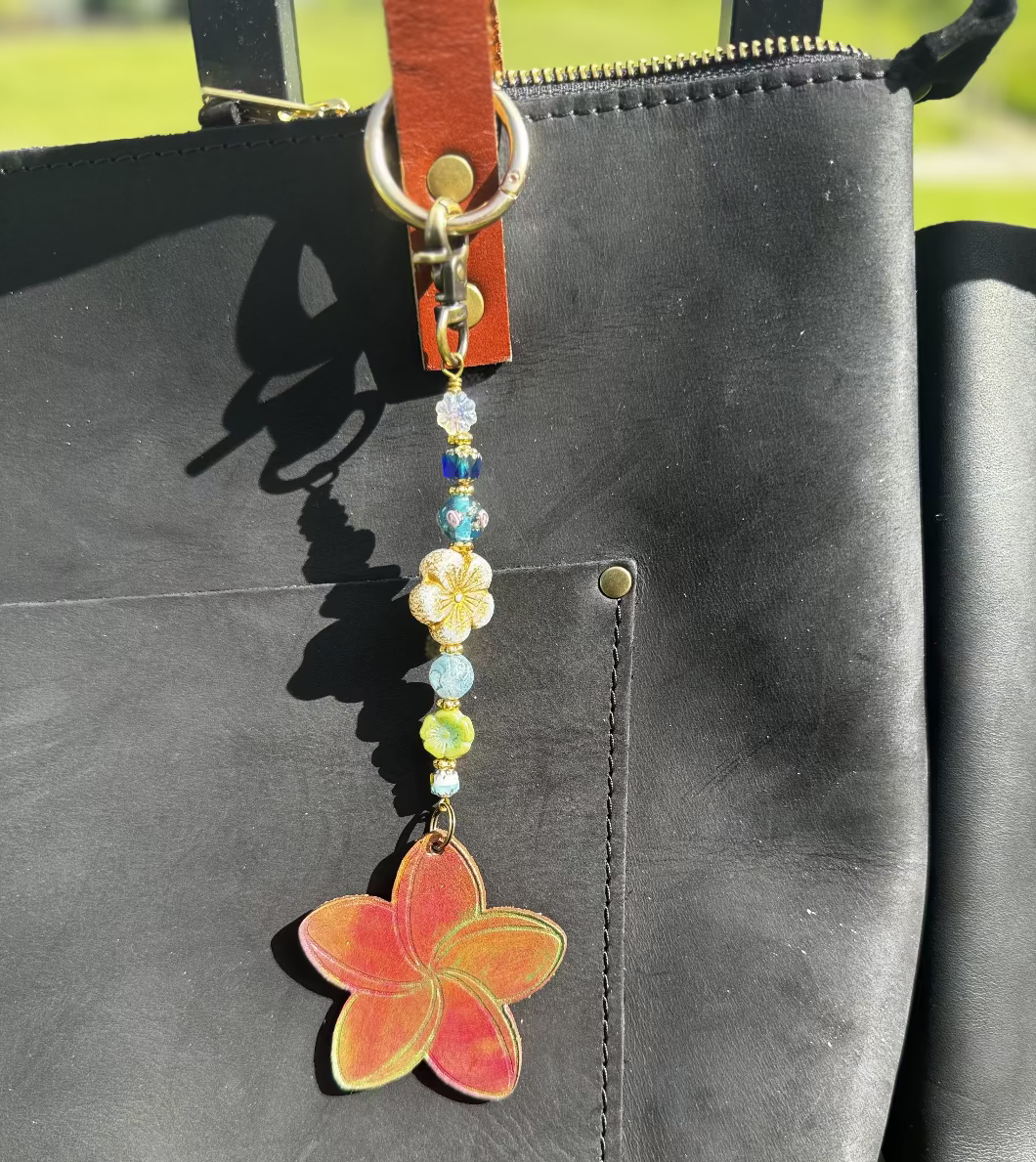 Decorative keychain with colorful beads and a red flower charm on a black bag.