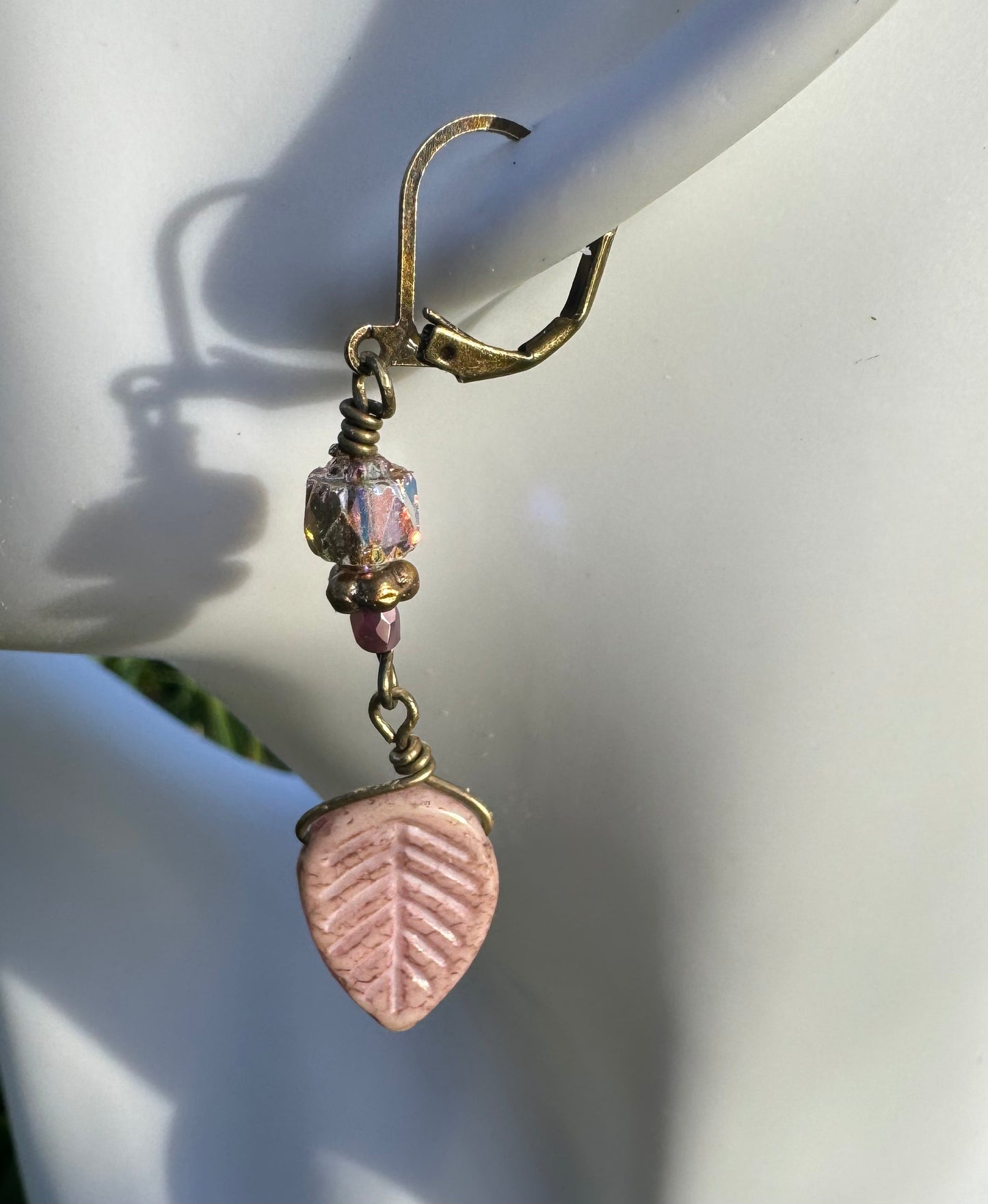 Handmade with Czech glass beads, these earrings have a celestial glow. They feature an antique bronze finish and brass hardware, including a leaf-shaped charm.