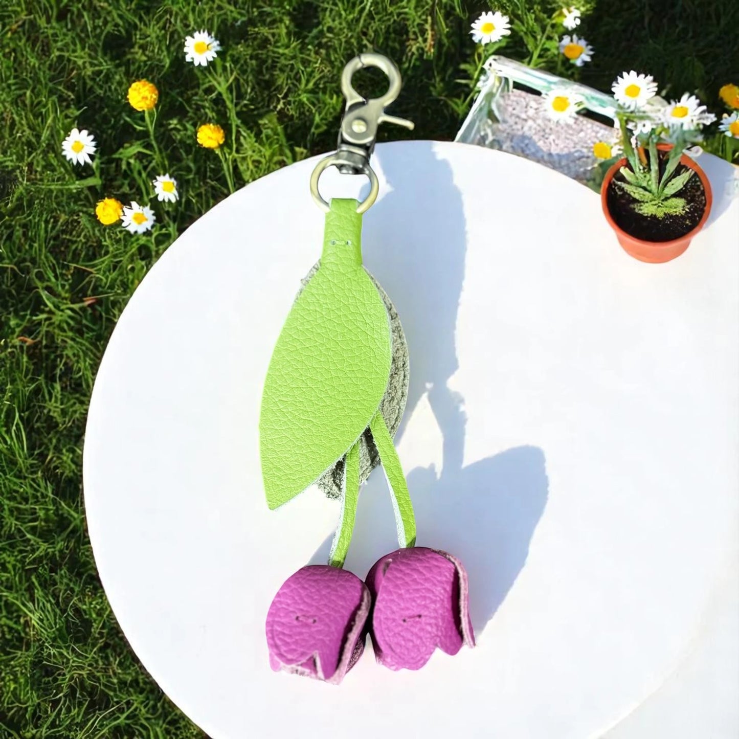 Green and purple keychain on a white surface with grass and flowers in the background