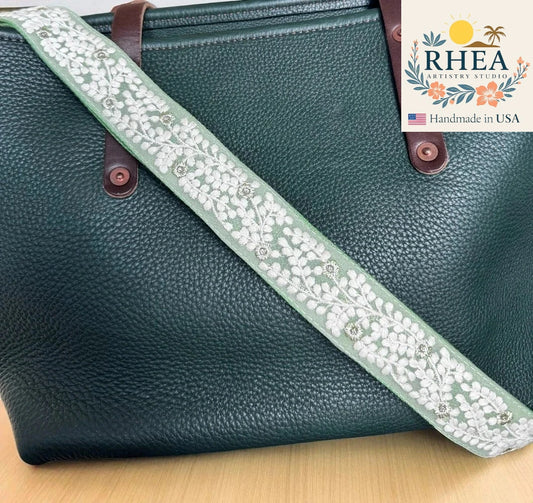 Green leather bag with a floral strap on a wooden surface, featuring the RHEA Artistry Studio logo.