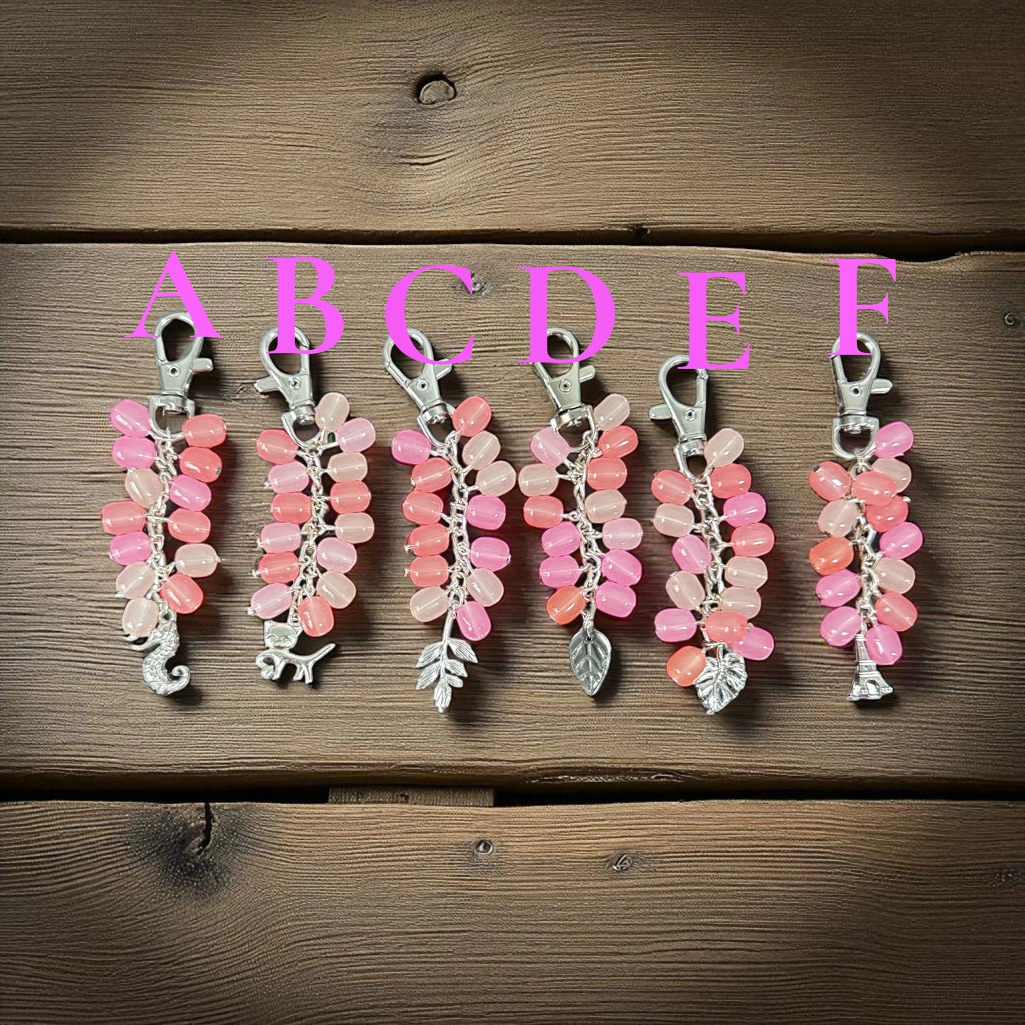 Set of pink and silver keychains on a wooden surface with letters A to F above them.