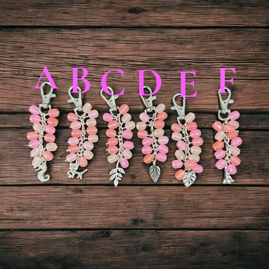 Set of six pink and white keychains on a wooden surface with letters above them.