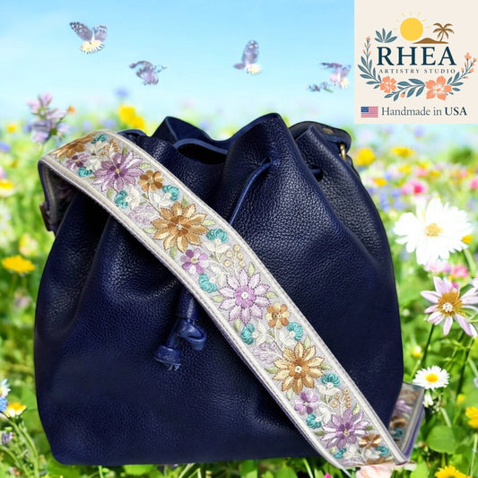 Navy blue handbag with floral purse strap against a floral background, featuring the RHEEA brand.