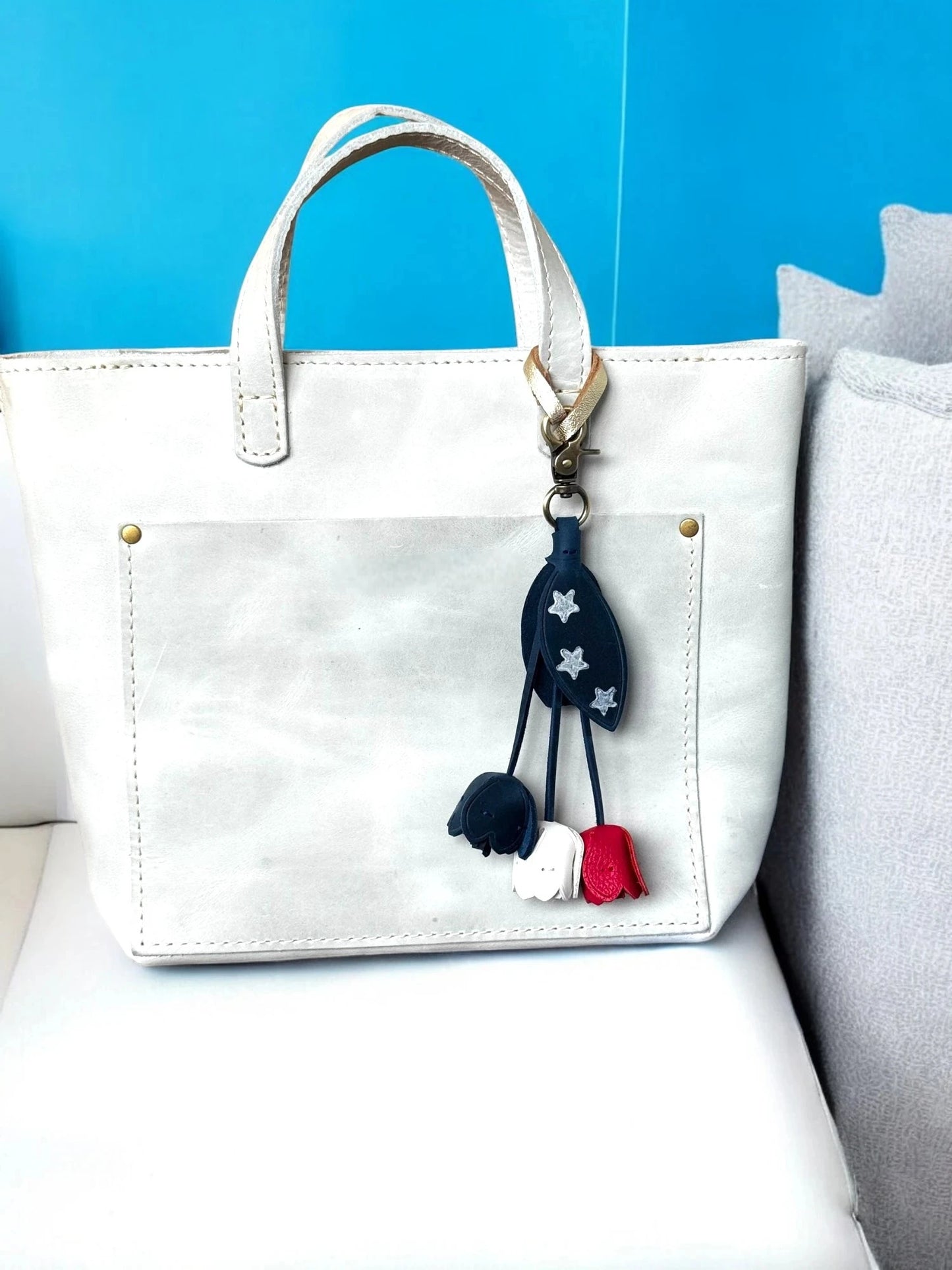 White handbag with decorative keychain on a blue and gray background