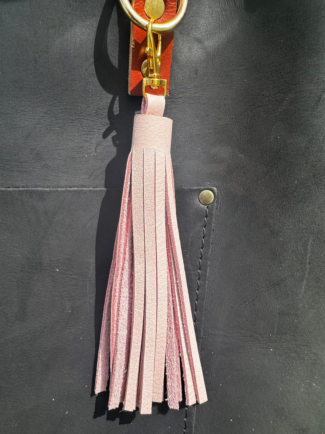 A pink leather tassel hanging from a red and black handbag on a grassy background.