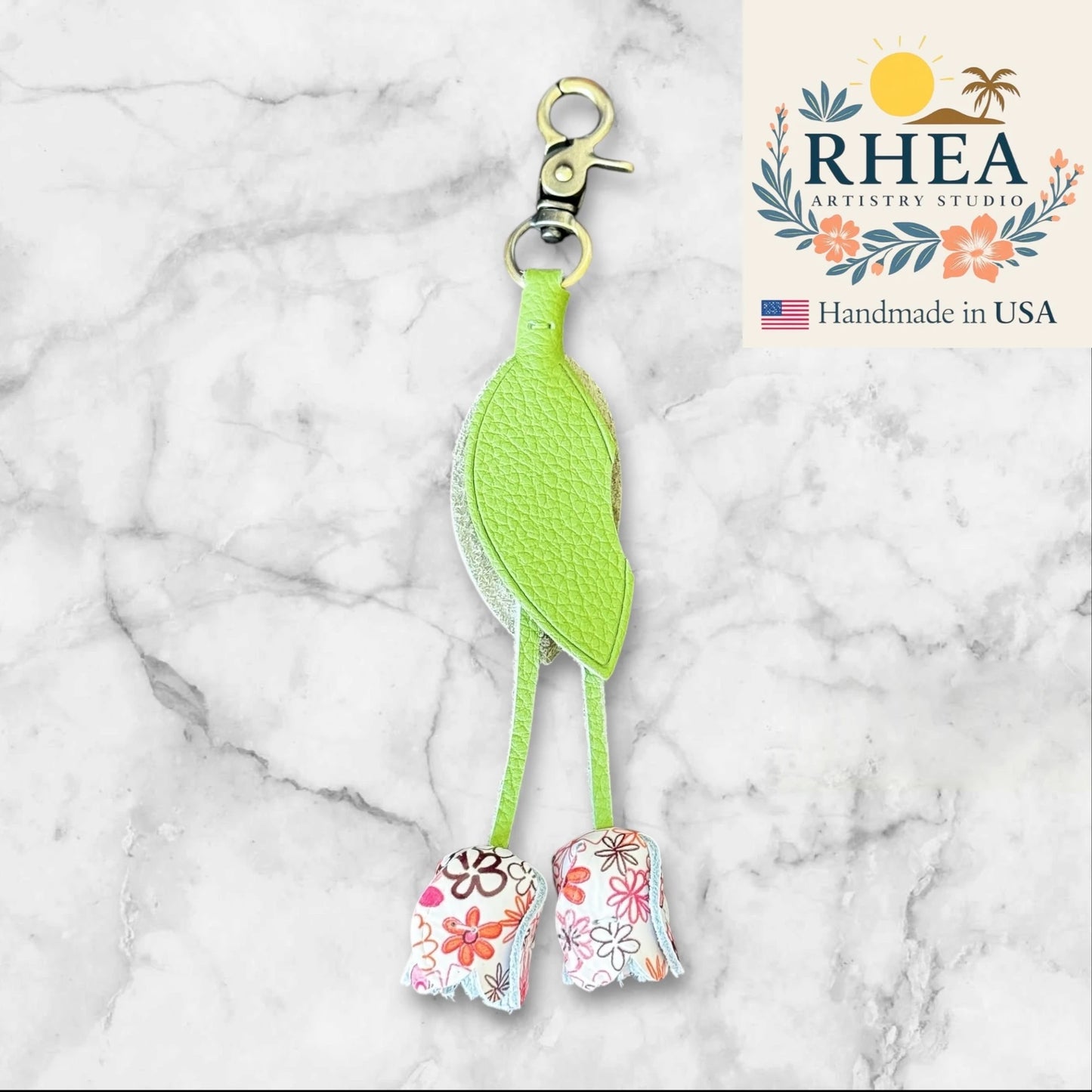 Green keychain with floral leather purse charm on a marble background, featuring RHEA Artistry Studio branding.