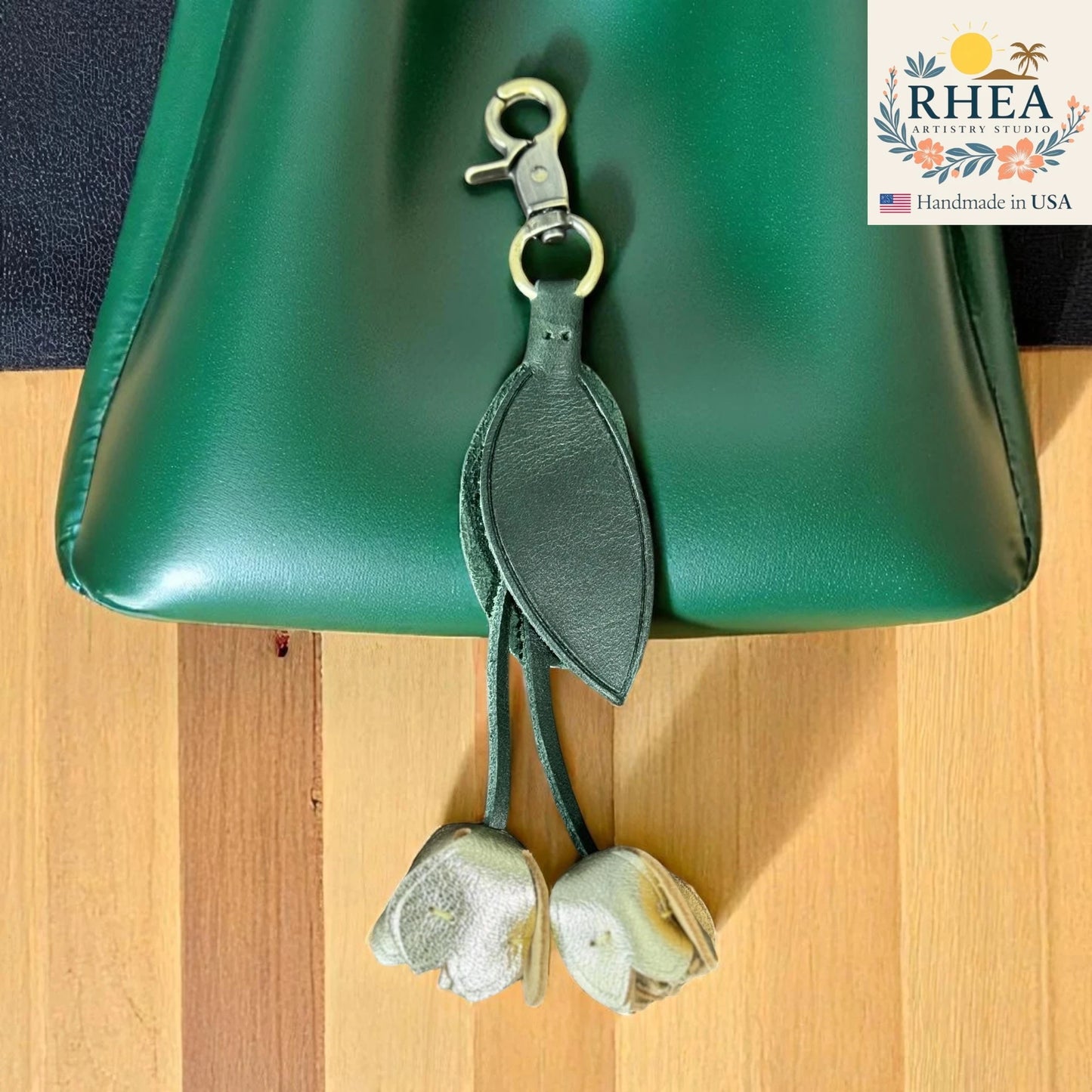 Green leather kleather purse charm attached to a green bag on a wooden surface, with RHEA branding visible.