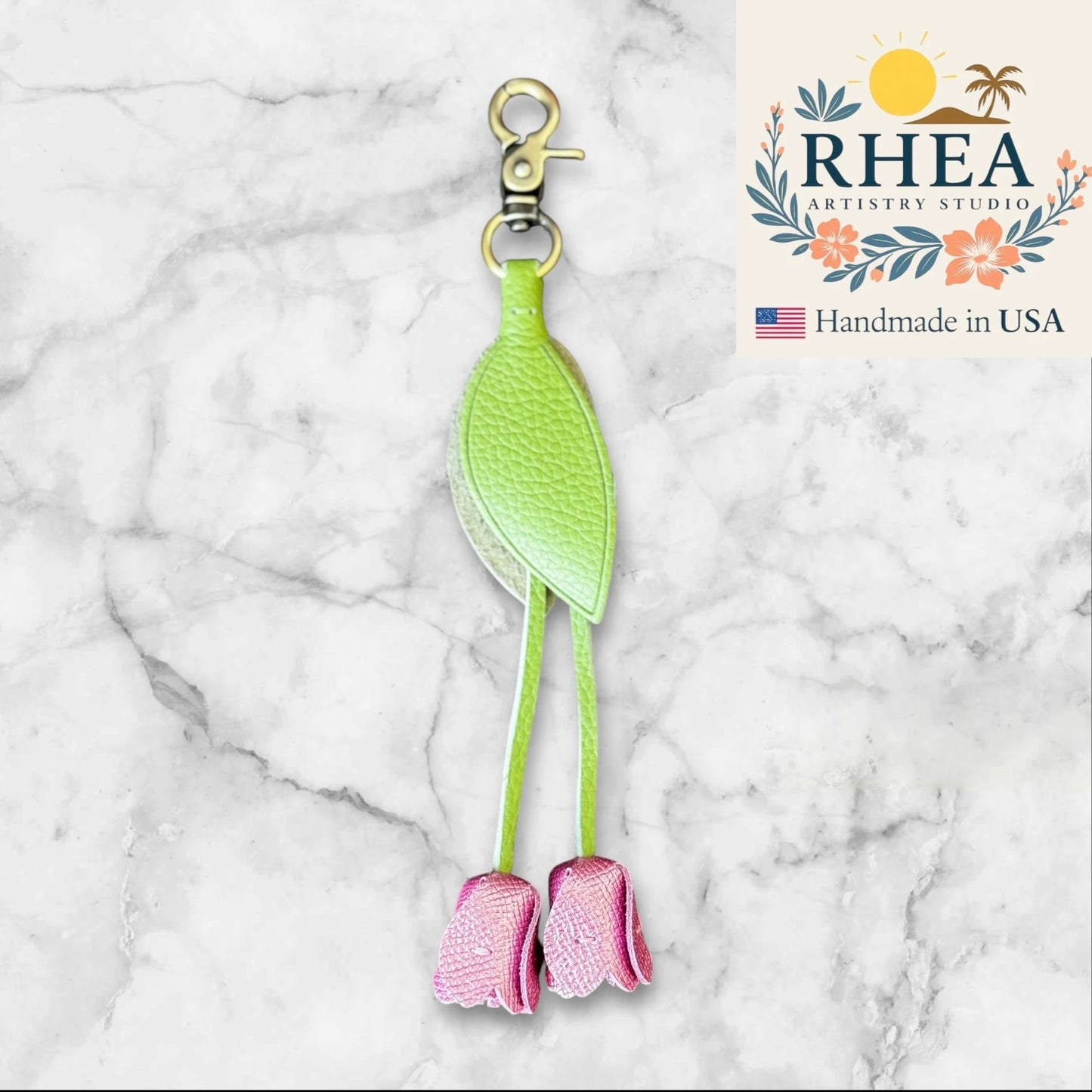 Green and pink leather purse charm with RHEA Artistry Studio branding on a marble background