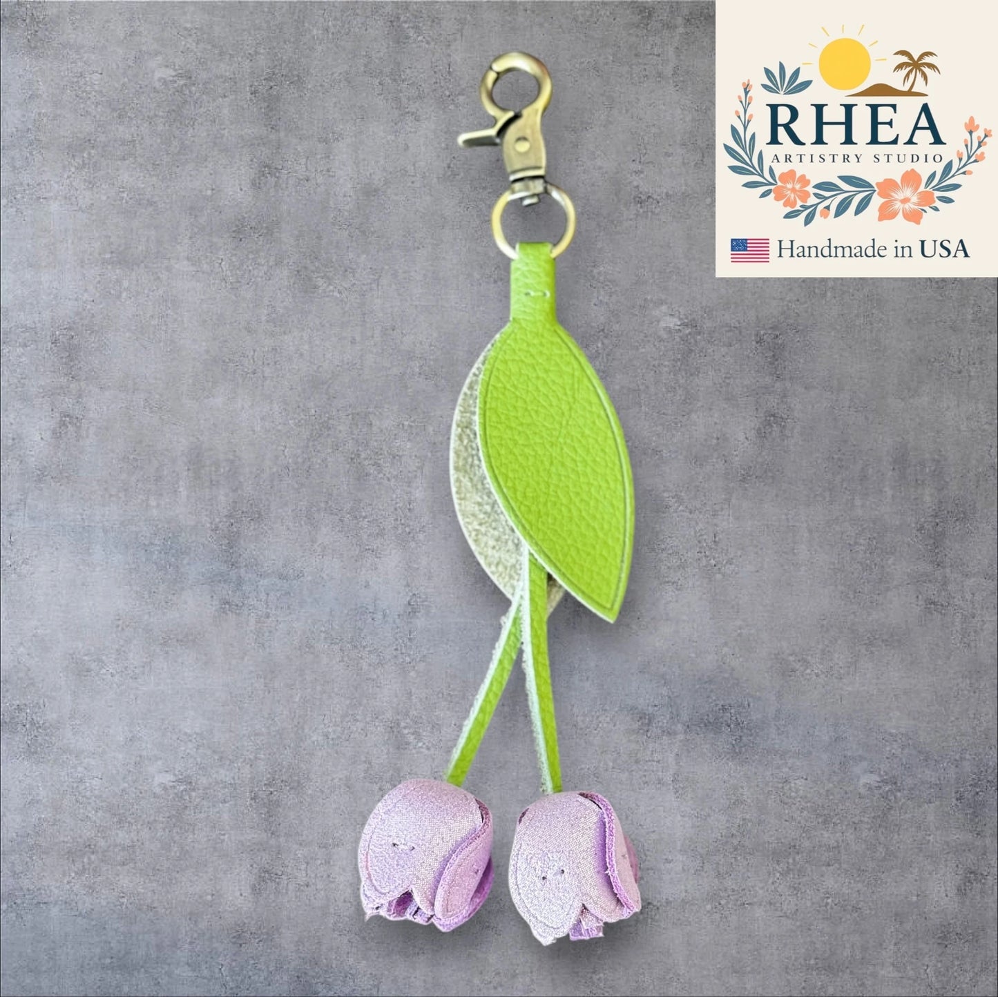 Green leaf and purple flower leather purse charm on a gray background with RHEA Artistry Studio branding.