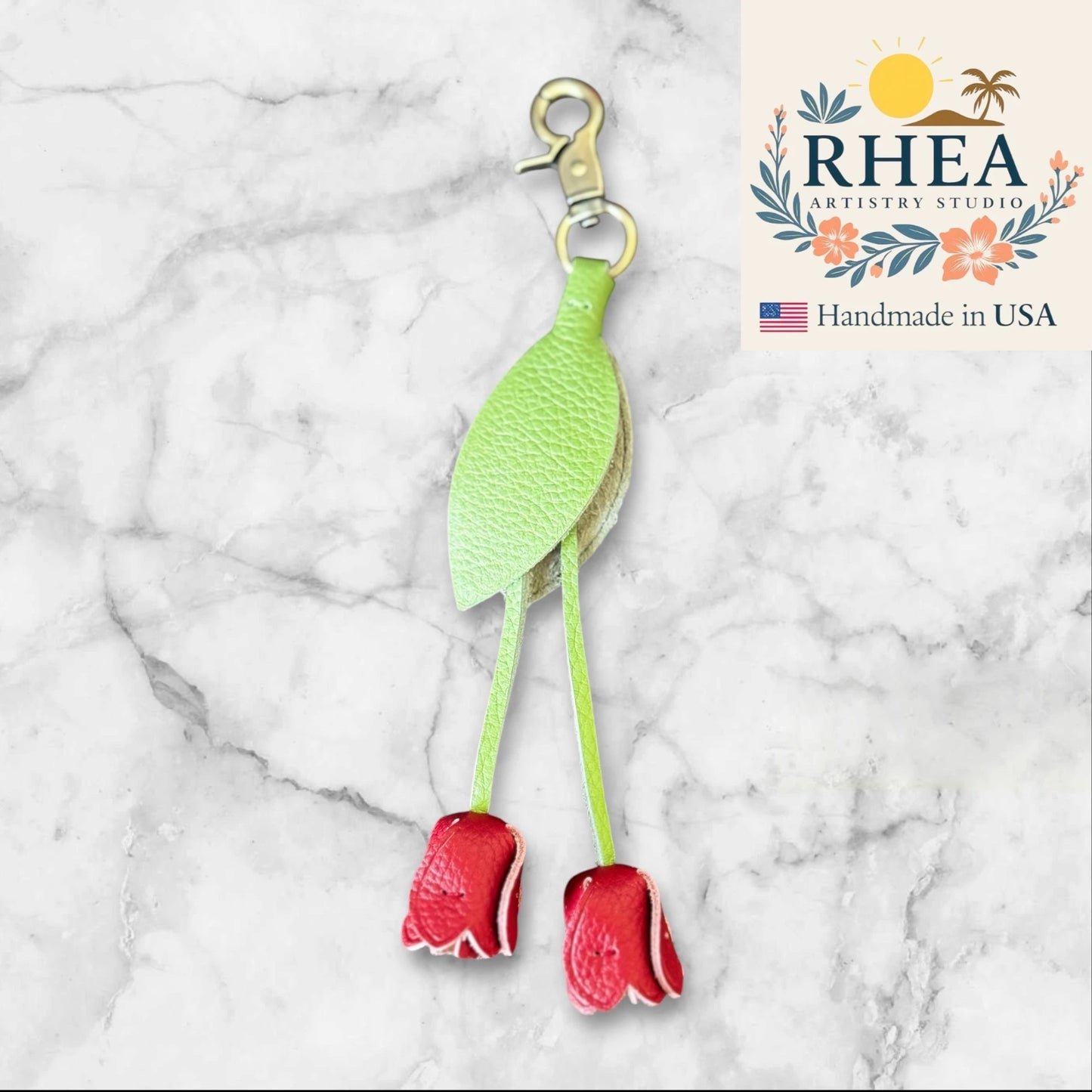 Green and red floral leather purse charm on a marble background with RHEA Artistry Studio branding.