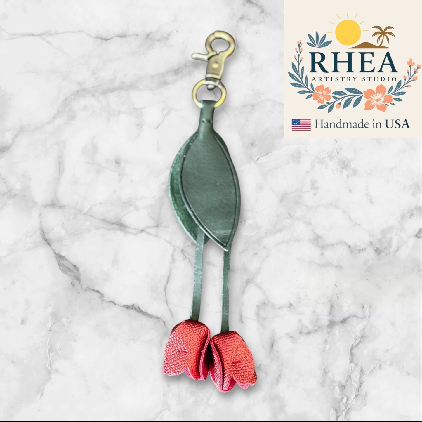 Green and pink leather purse charm with RHEA Artistry Studio logo on a marble background