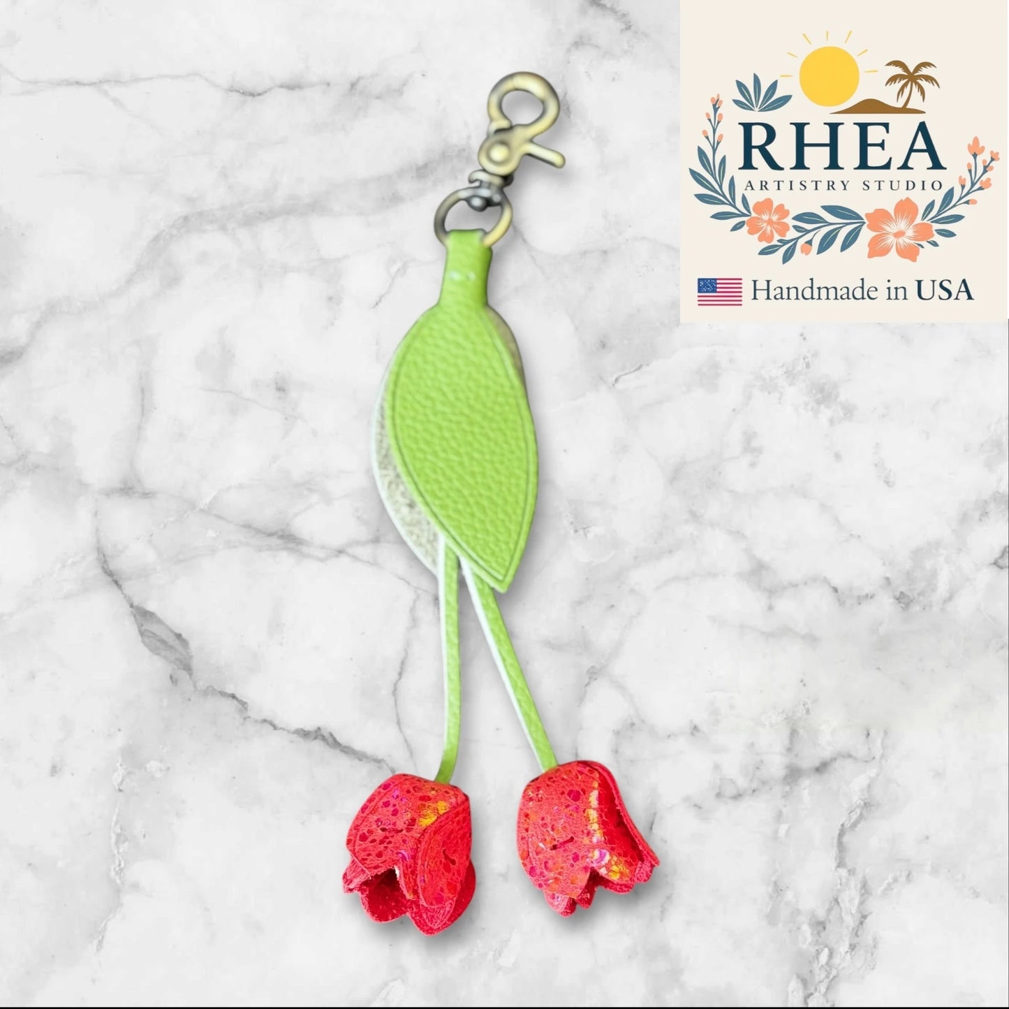 Green leather purse charm with red floral charms on a marble background, featuring RHEA Artistry Studio branding.