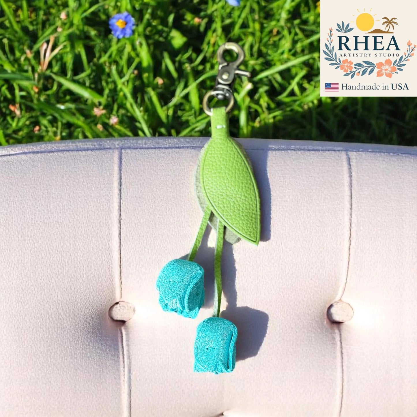 Green and blue leather purse charm with RHEA Artisan Studio branding on a grassy background