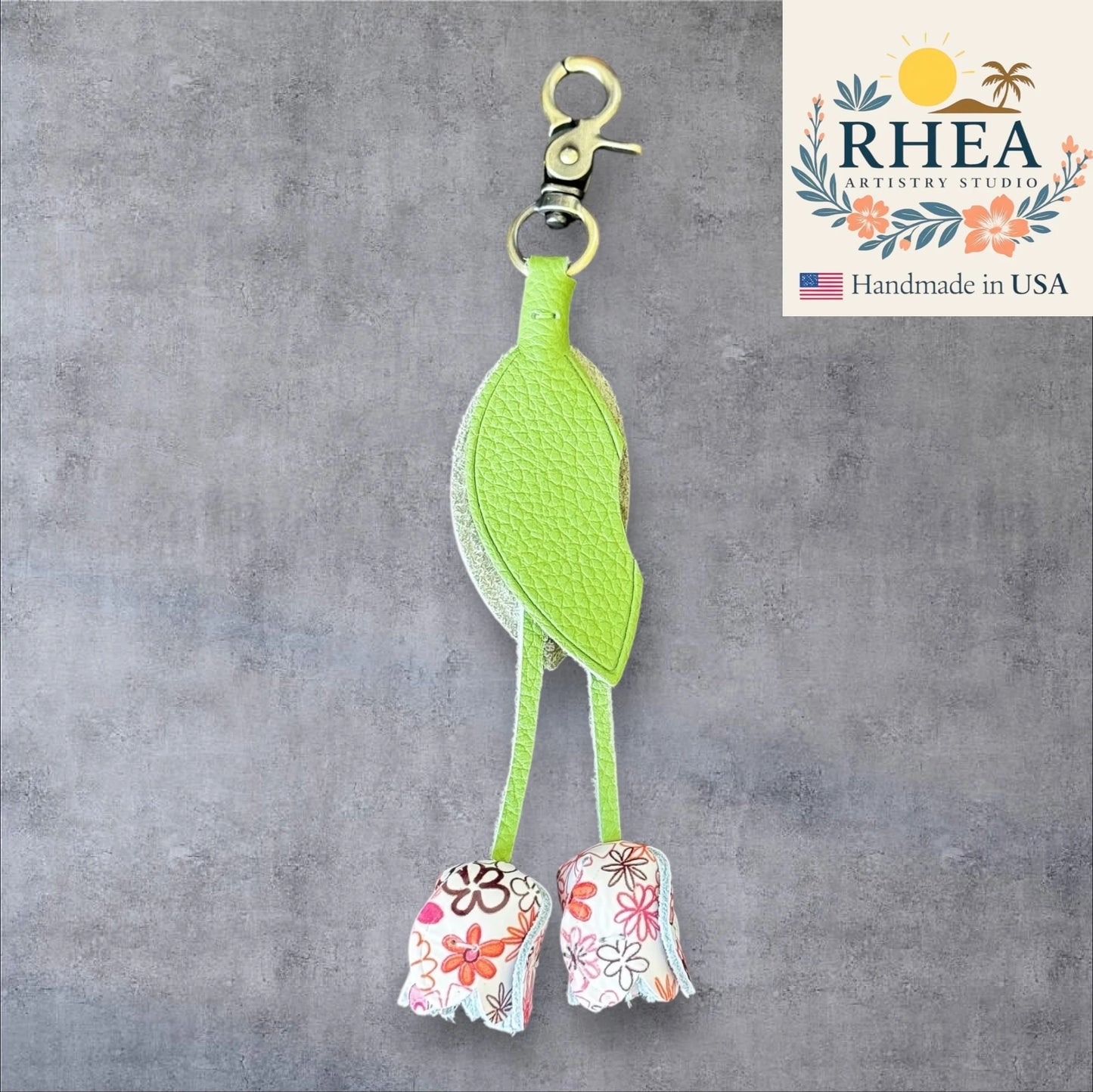 Green leather purse charm with floral designs on a gray background, featuring the RHEA Artistry Studio logo.