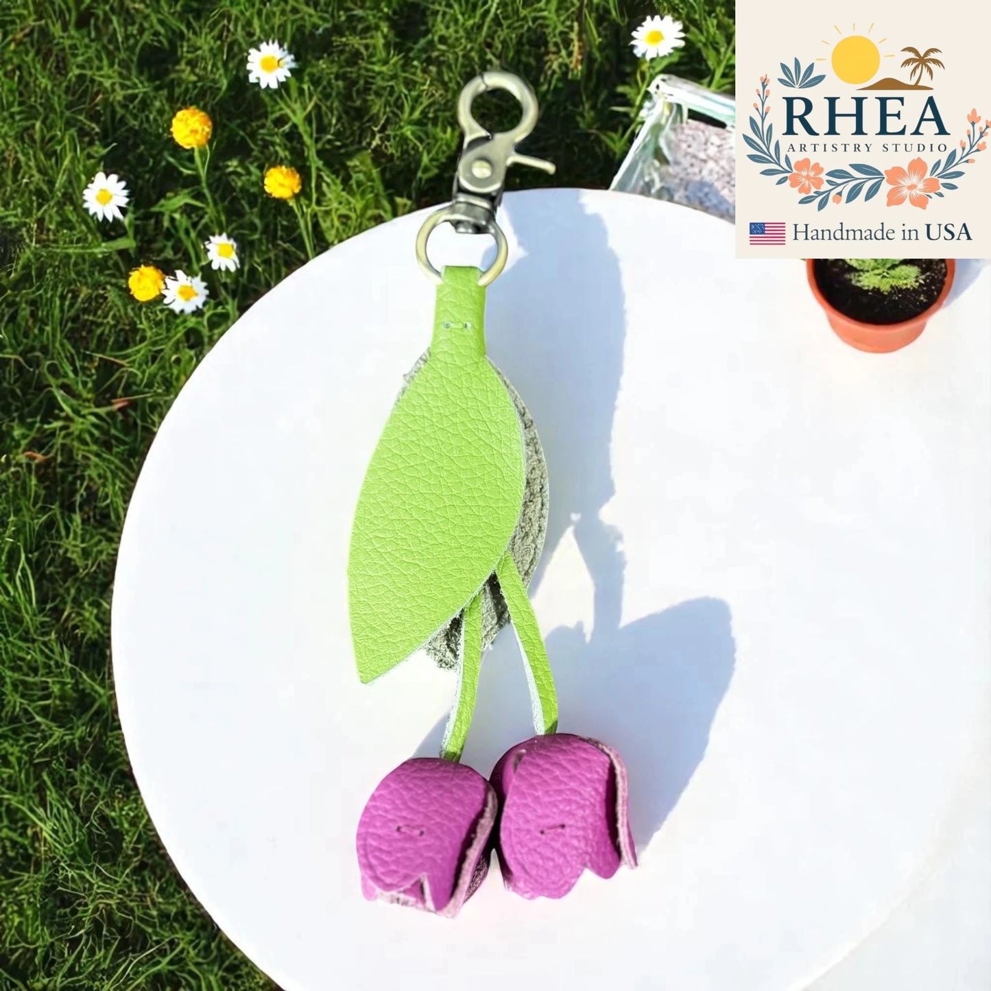 Green and purple leather purse charm with RHEA branding on a white plate outdoors.