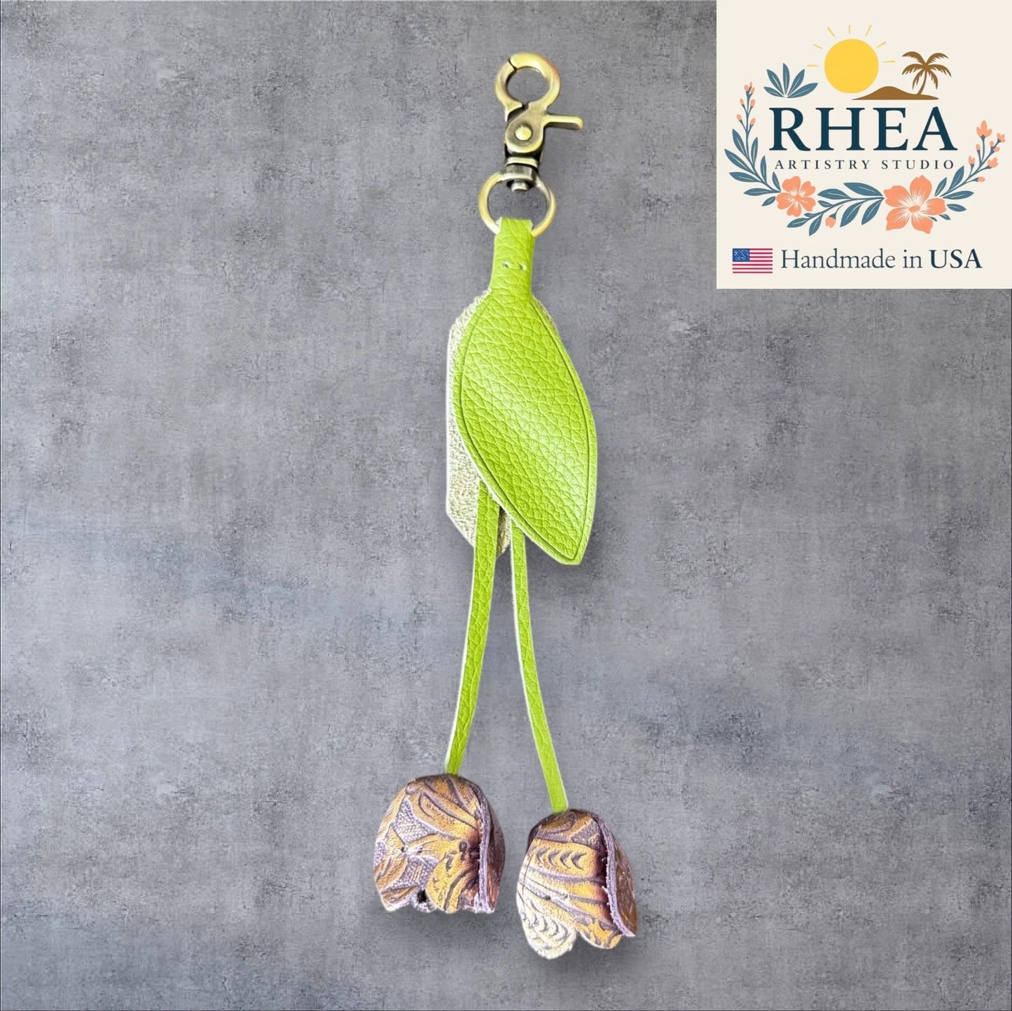 Green bird-shaped leather purse charm with decorative elements on a gray background, featuring the RHEA Artistry Studio logo.