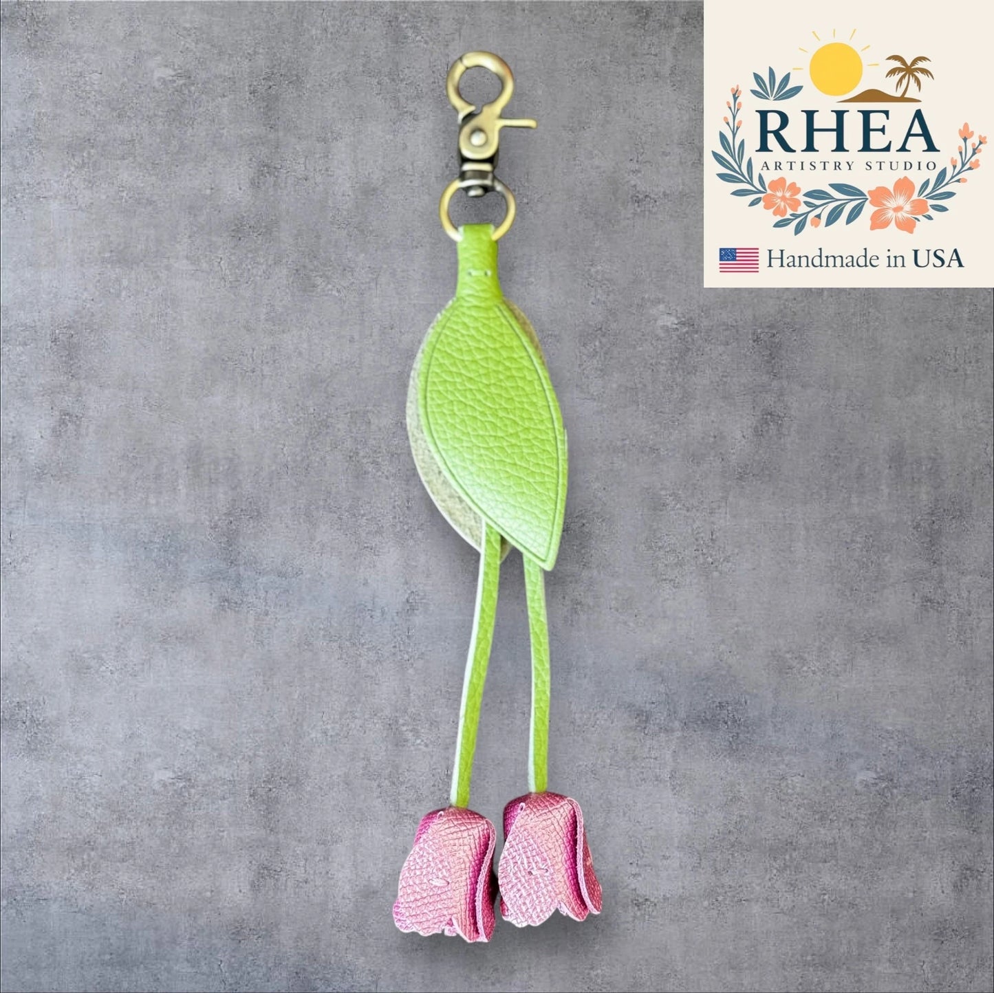 Green and pink leather purse charm with 'RHEA Artistry Studio' branding on a gray background