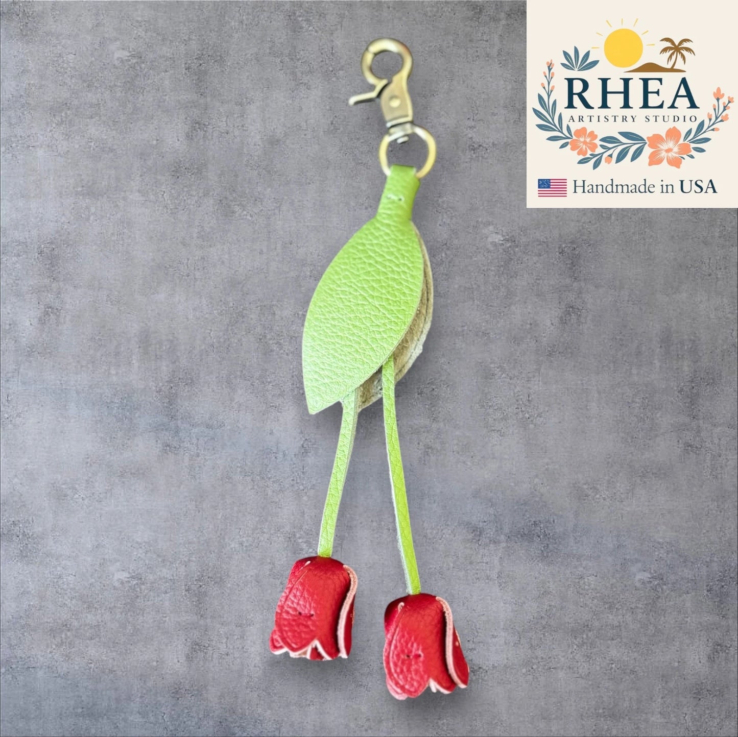 Green leaf-shaped leather purse charm with red flowers on a gray background, branded 'RHEA Artistry Studio'.
