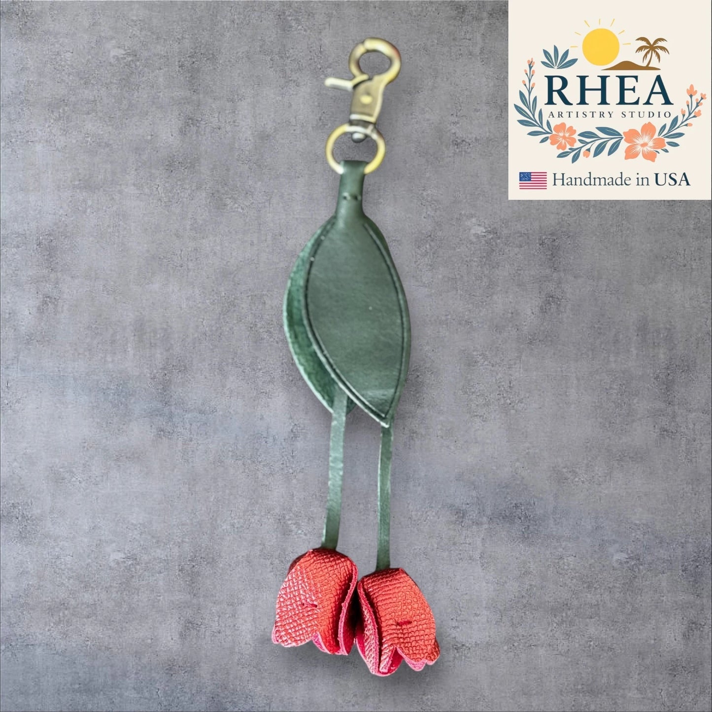 Green and red leather purse charm with RHEA Artistry Studio logo on a gray background