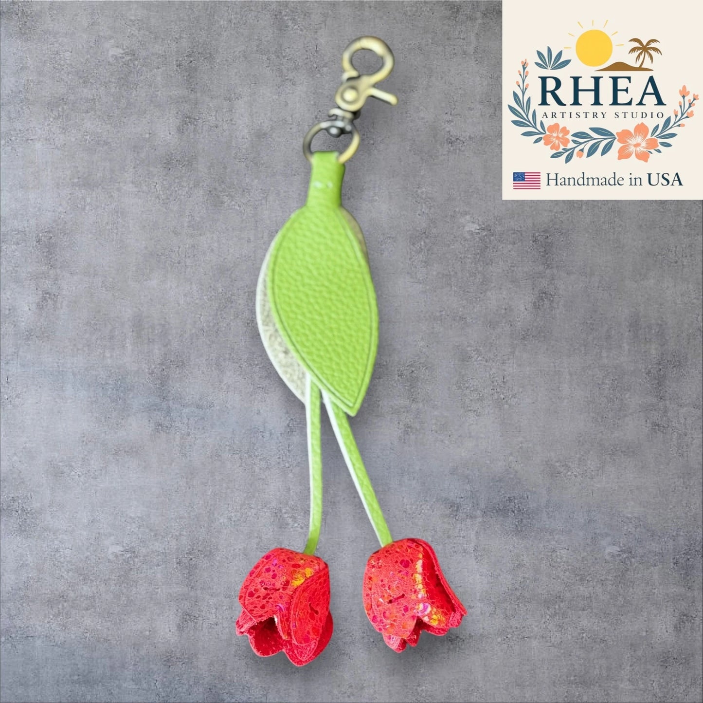 Green and red leather purse charm with 'RHEA Artistry Studio' logo on a gray background