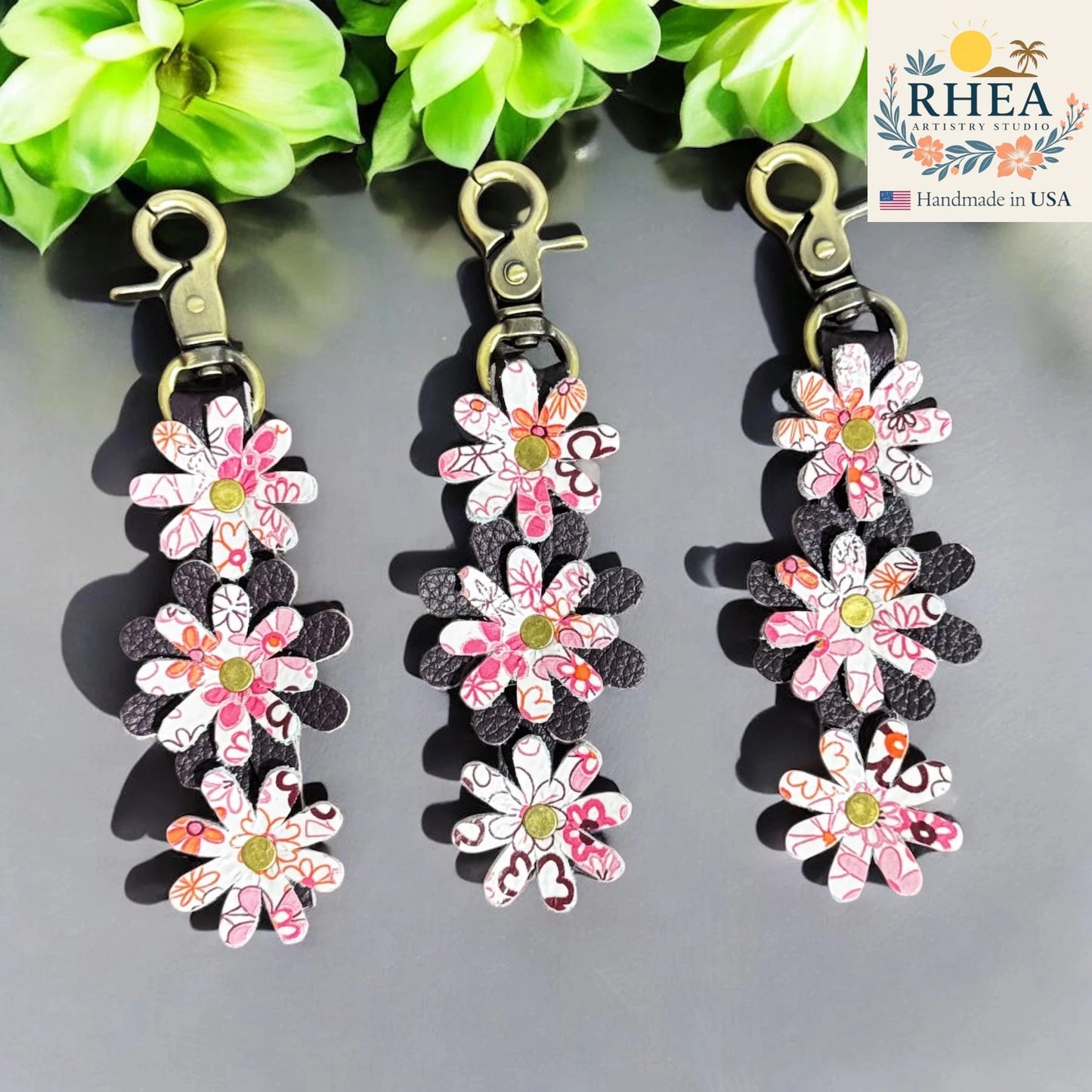 Floral leather bag charms with a RHEA Artistry Studios logo in the corner.