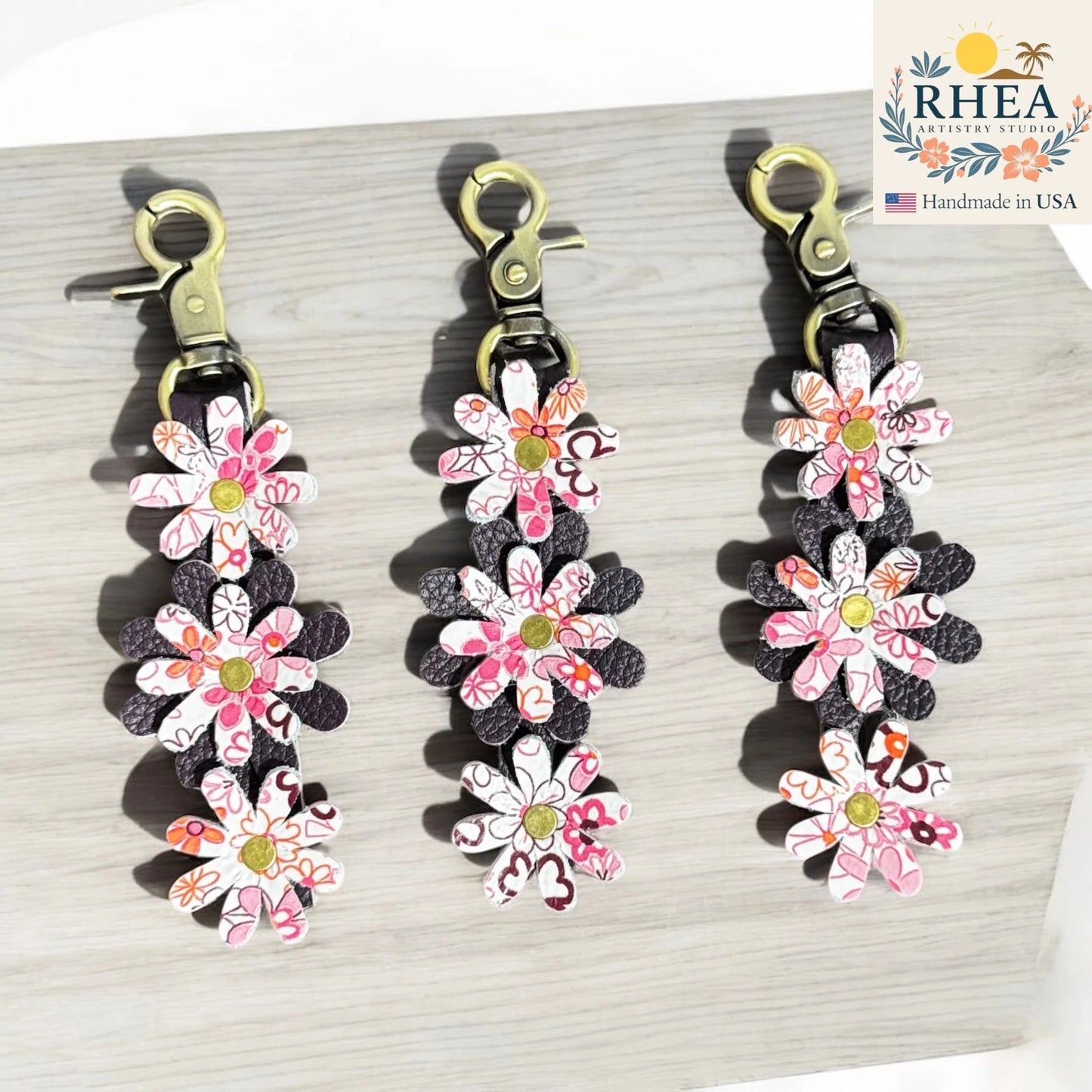 Floral leather bag charms with RHEA Artistry Studio branding on a light wooden surface.