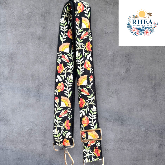 An adjustable embroidered purse strap with a floral pattern and gold hardware, displayed against a grey background.