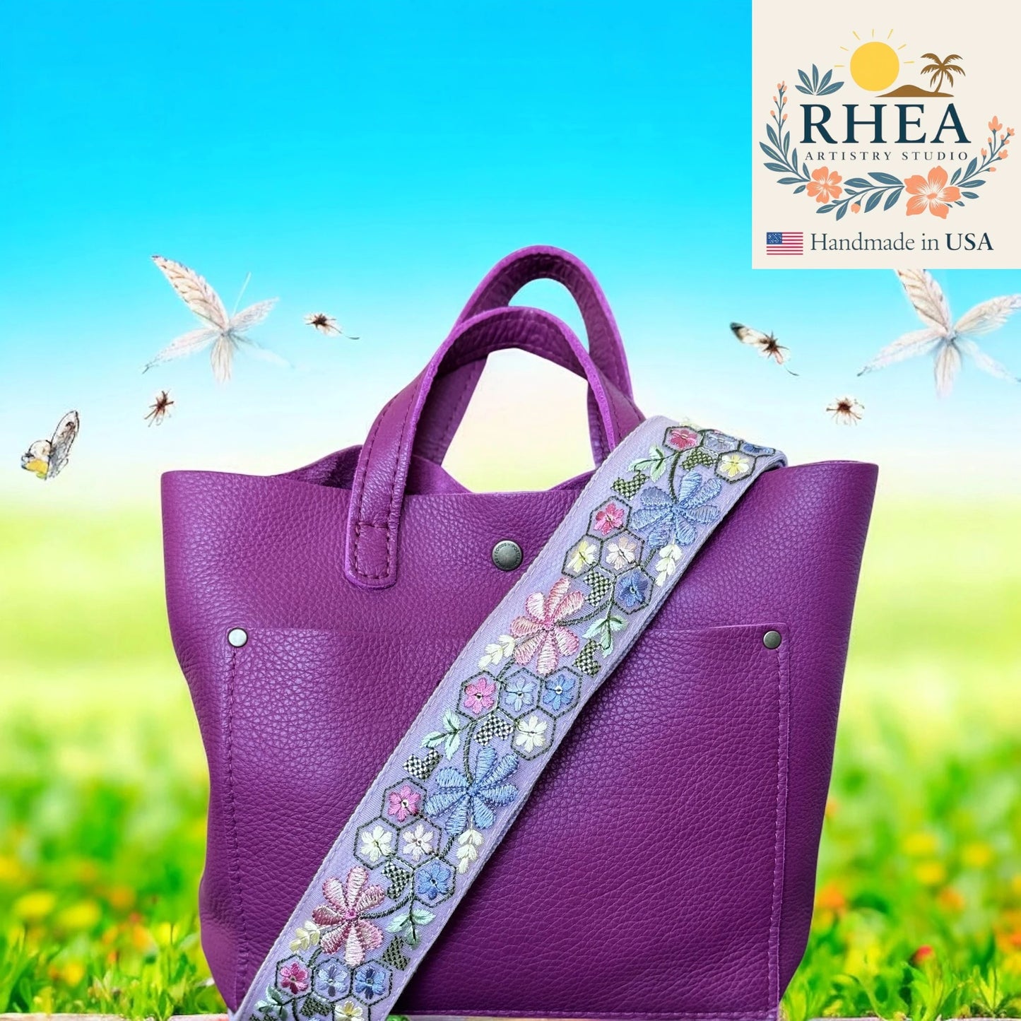 Purple handbag with a floral strap on a grassy background, featuring the RHEA Artistry Studio logo.