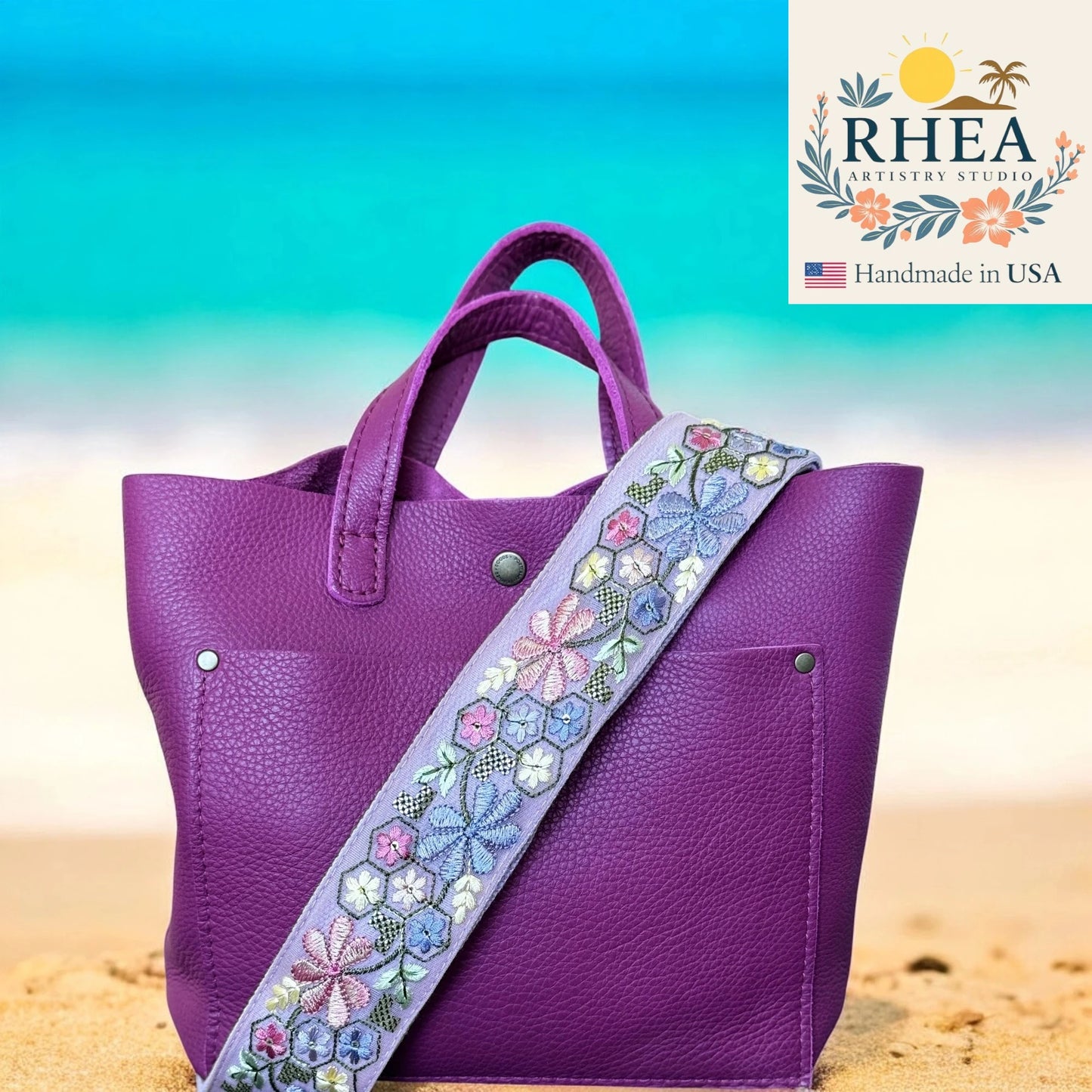 Purple handbag with a floral strap on a beach background, featuring the RHEA Artistry Studio logo.