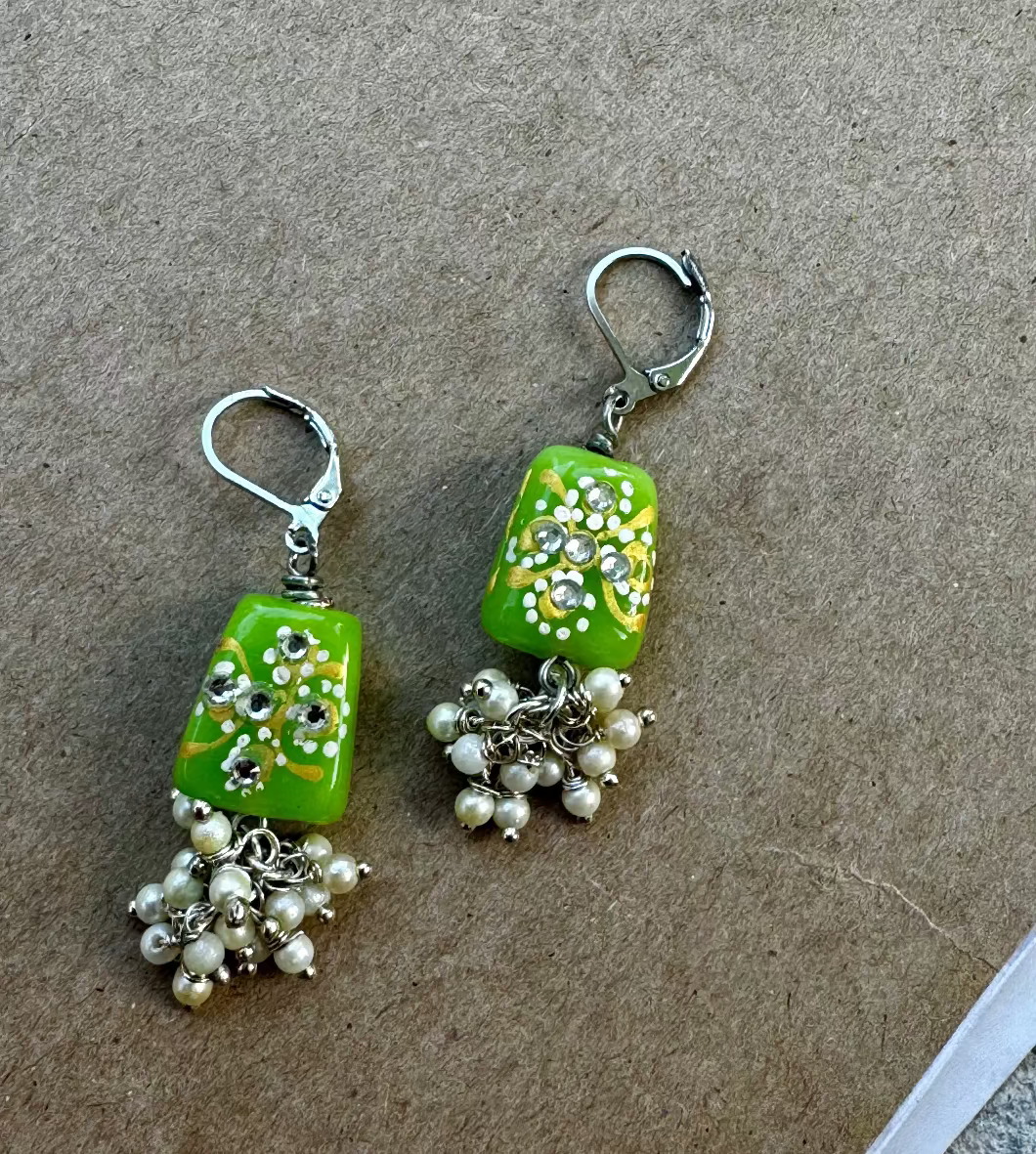 A pair of lime green pearl cluster silver earrings with a drop design and French lever back closure, displayed against a brown background.