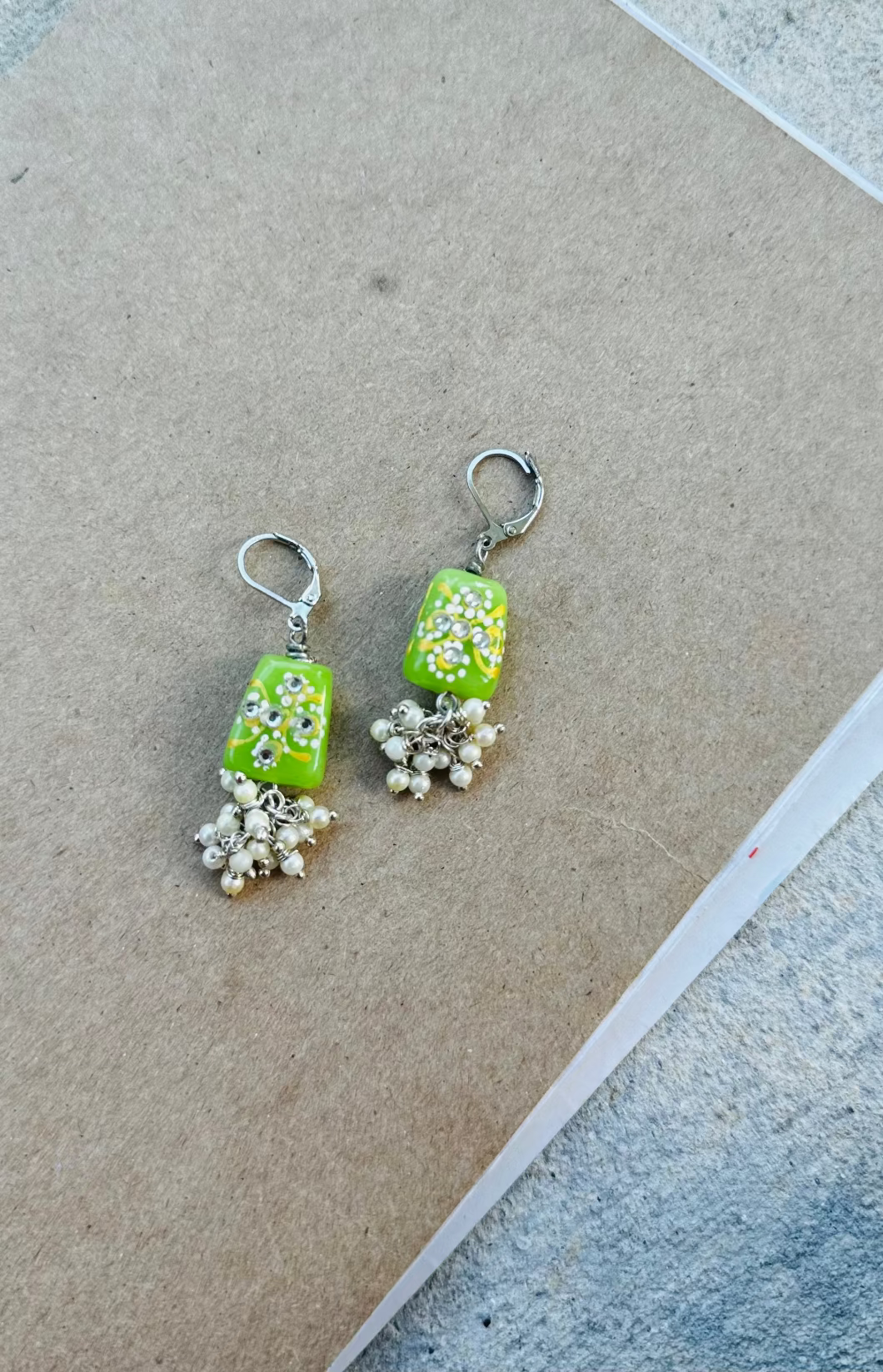 A pair of lime green pearl cluster silver earrings with a drop design and French lever back closure, displayed against a brown background.