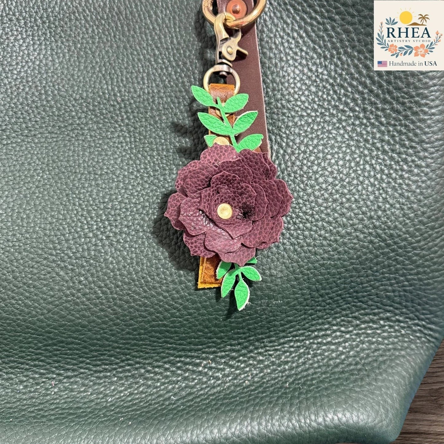 Floral keychain attached to a green textured surface with RHEA branding.