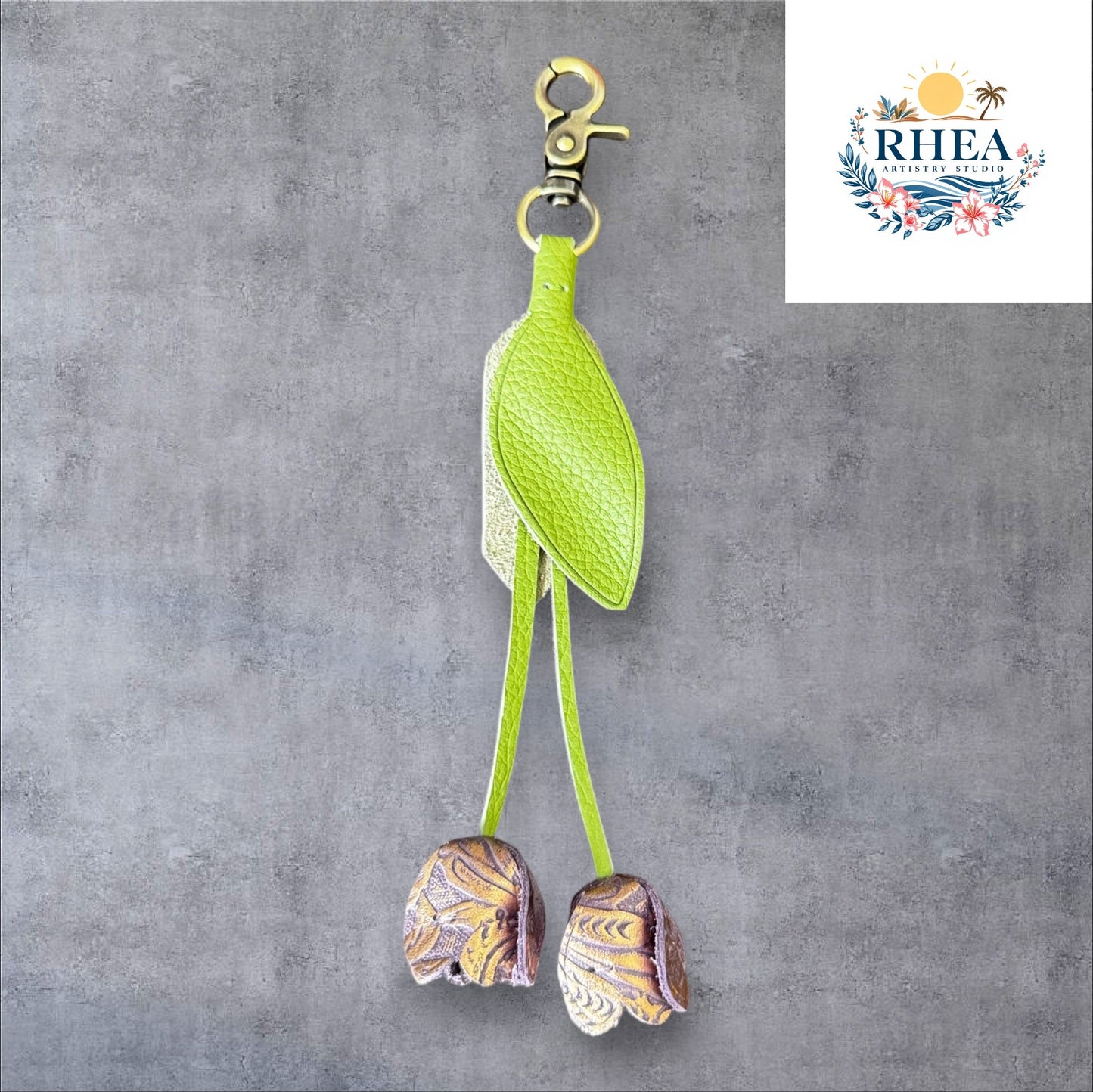 A handmade leather tulip charm with a green leaf and brown floral pattern, attached to a gold lobster clasp on a white marble surface.
