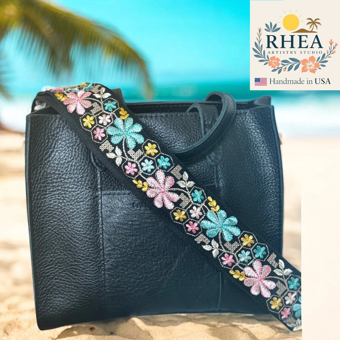 Black leather bag with an embroidered floral strap on a beach background, featuring the RHEA Artistry Studio logo.