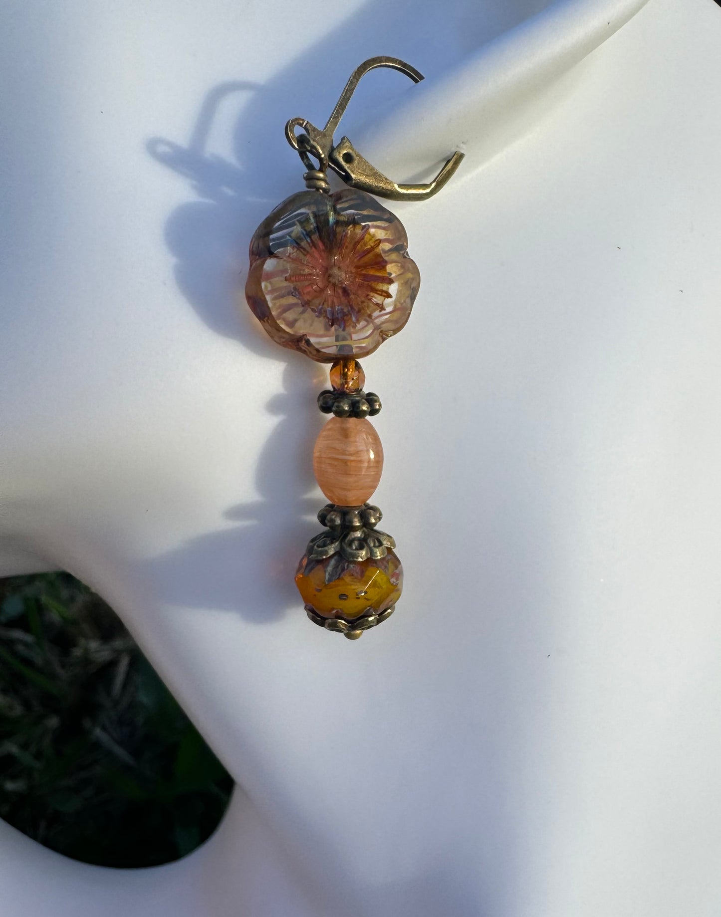 A pair of mustard yellow glass hibiscus flower drop earrings with brass accents placed on a model