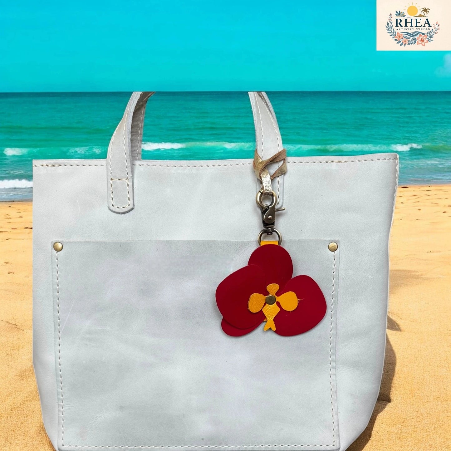 White tote bag with a red flower charm on a beach