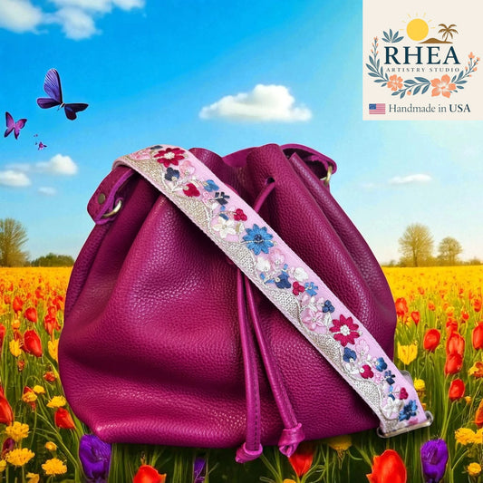 Purple leather bag with floral leather purse strap in a field of flowers and butterflies, RHEA brand visible.