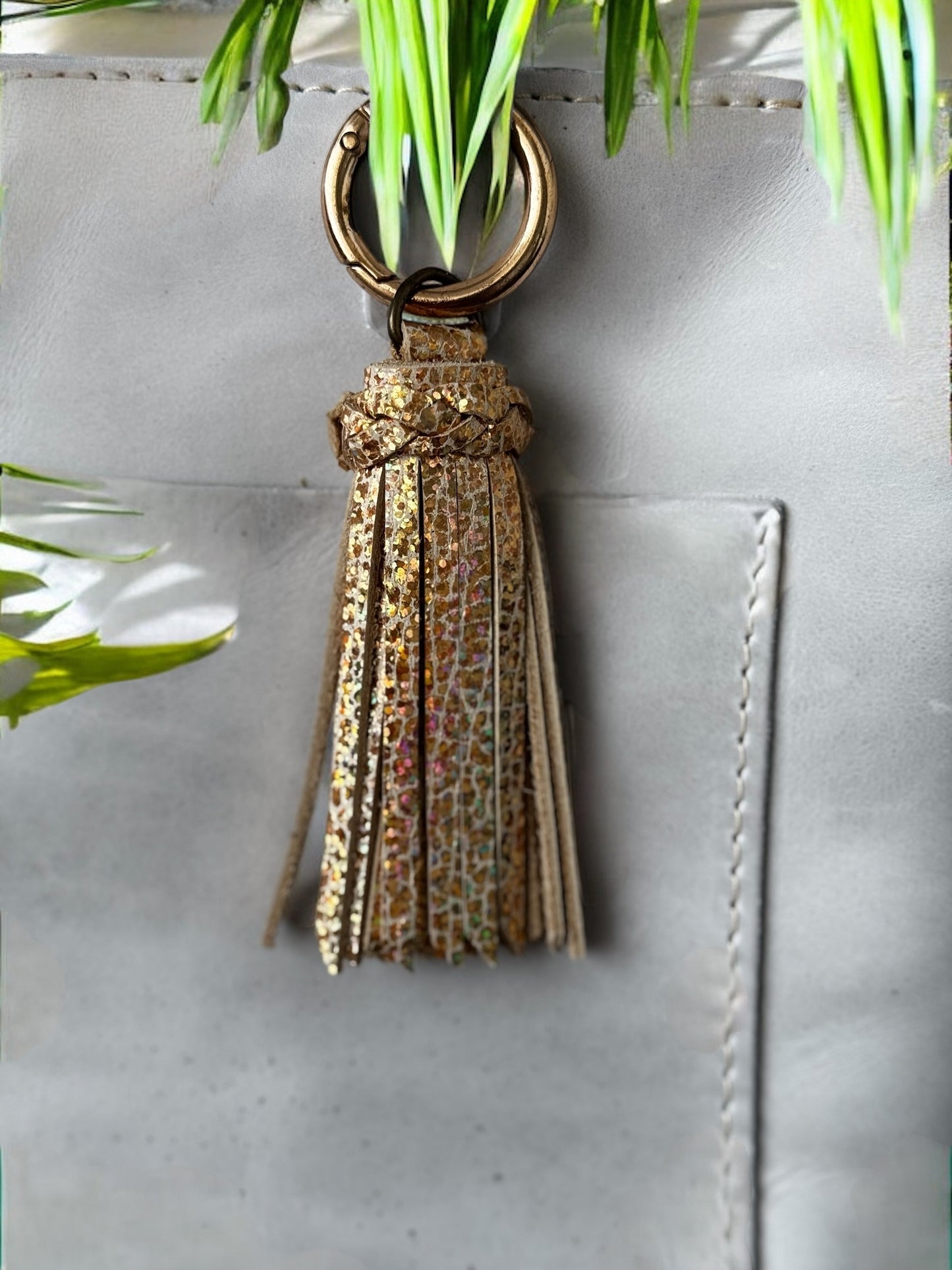 Gray handbag with a beige/gold tassel charm against a natural background