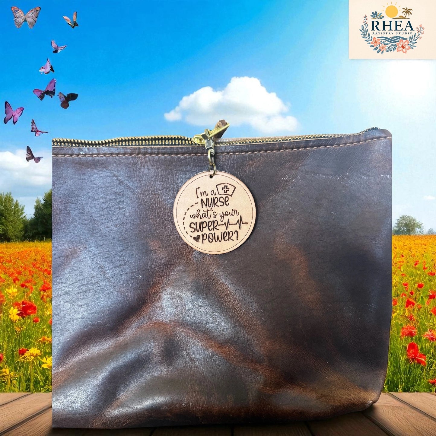 Brown leather pouch with a charm reading 'I'm a nurse, what's your super power?' against a scenic background with butterflies and flowers.