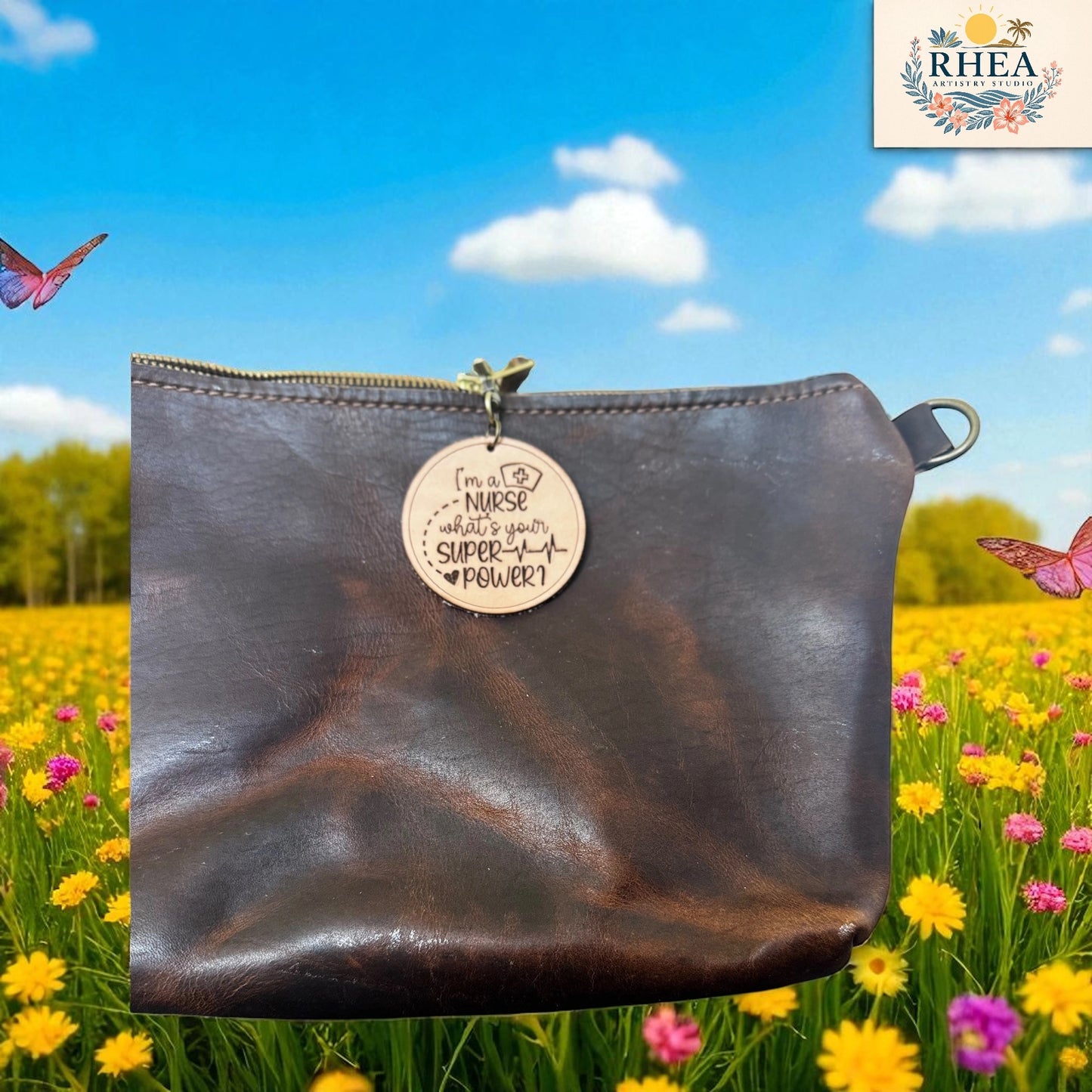 Brown leather pouch with a tag in a field of flowers and butterflies, with RHEEA branding.