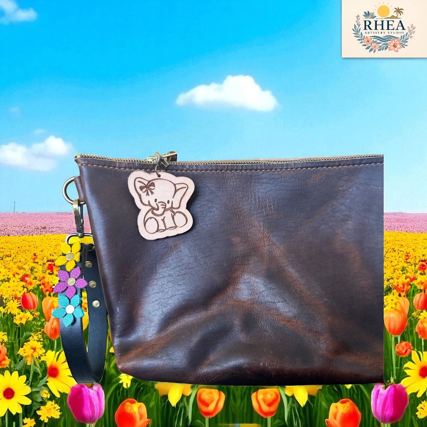 Brown leather pouch with a bear charm on a colorful floral background, featuring the RHEA brand.