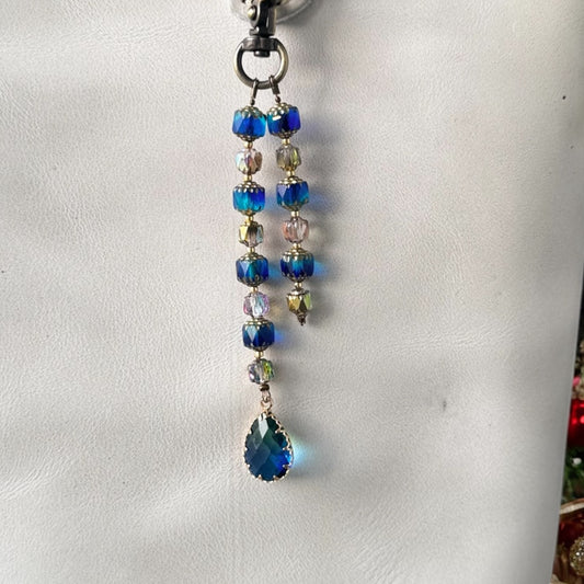 A white designer handbag with a crystal beaded keychain and a teardrop pendant, displayed against a festive background with Christmas decorations.